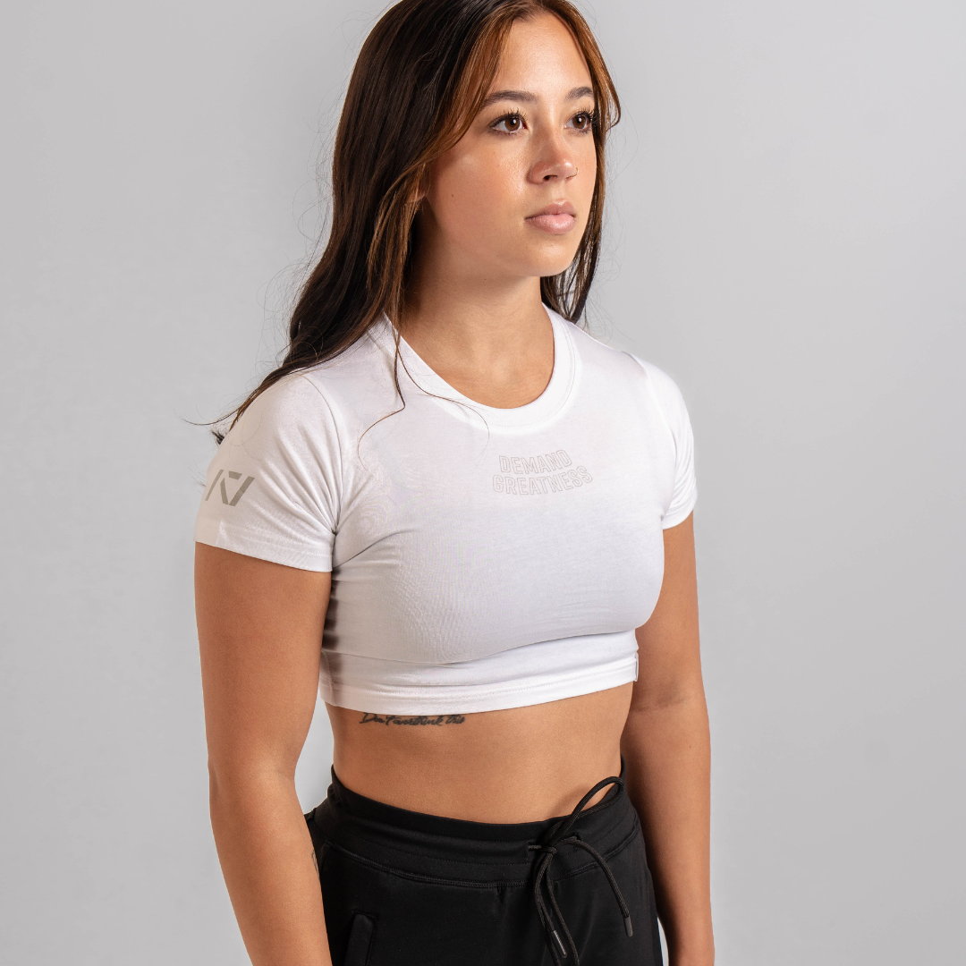 A woman wearing a white crop top with a Demand Greatness design on the upper chest and A7 logo on the upper back and sleeves.