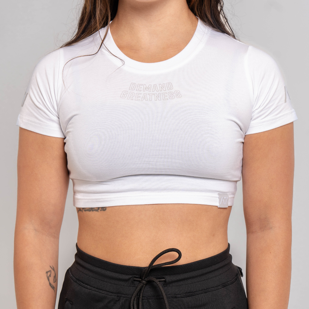 A woman wearing a white crop top with a Demand Greatness design on the upper chest and A7 logo on the upper back and sleeves.