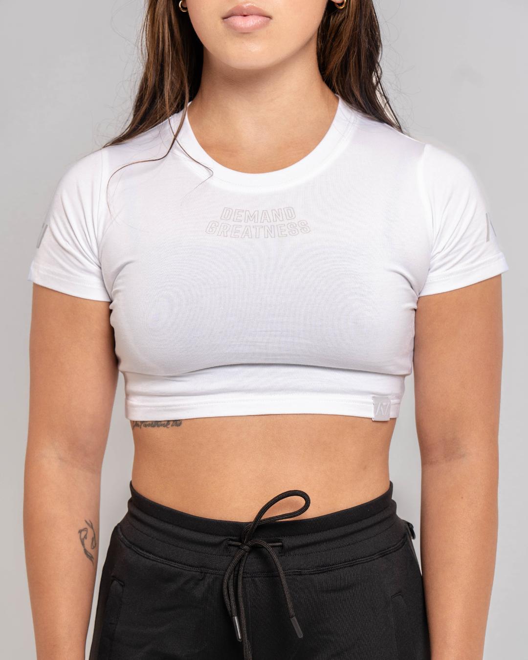 A woman wearing a white crop top with a Demand Greatness design on the upper chest and A7 logo on the upper back and sleeves.