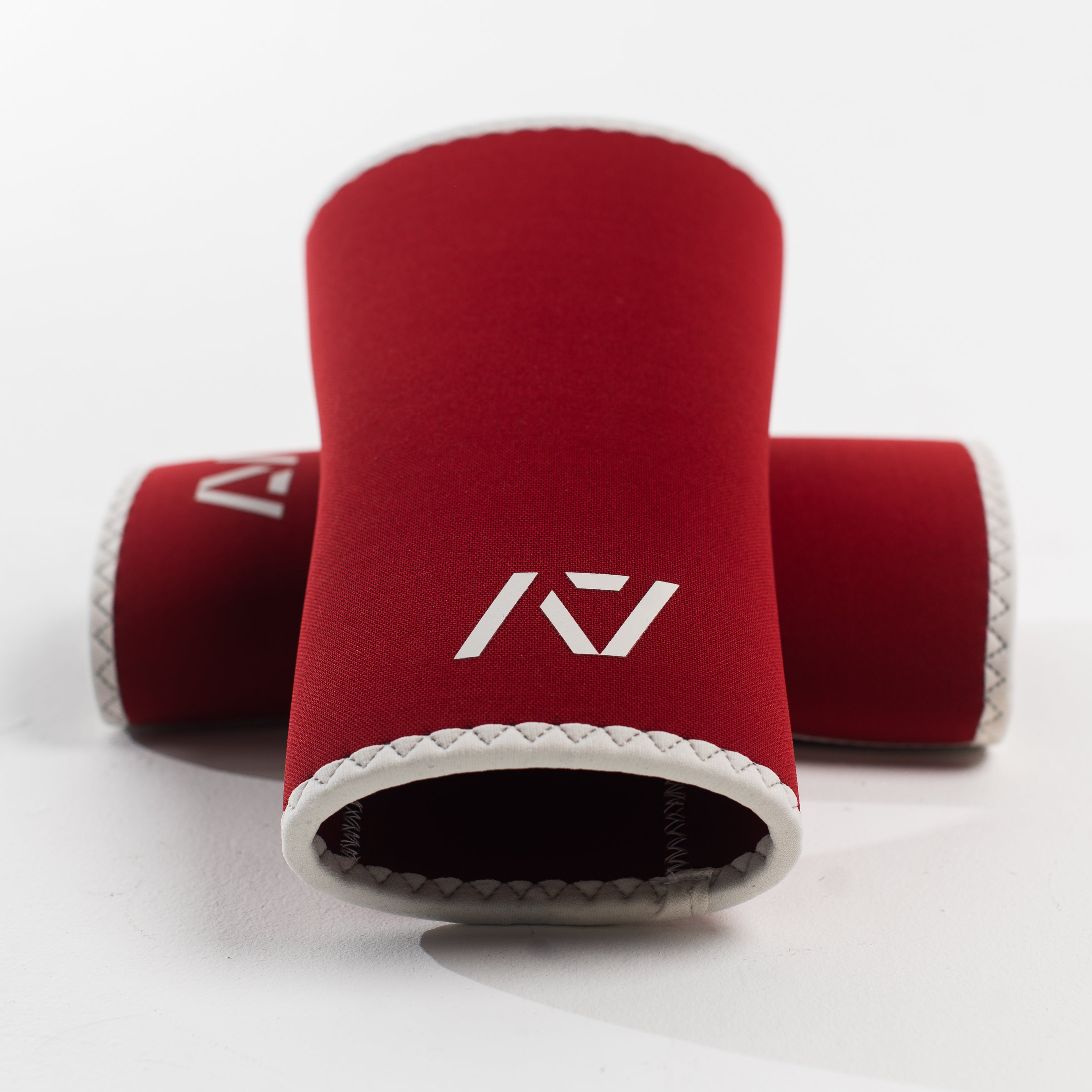 A pair of red knee sleeves with a white design that resembles a rose and tusk, symbolizing strength and beauty. The sleeves are designed with a hourglass-shaped center taper fit.