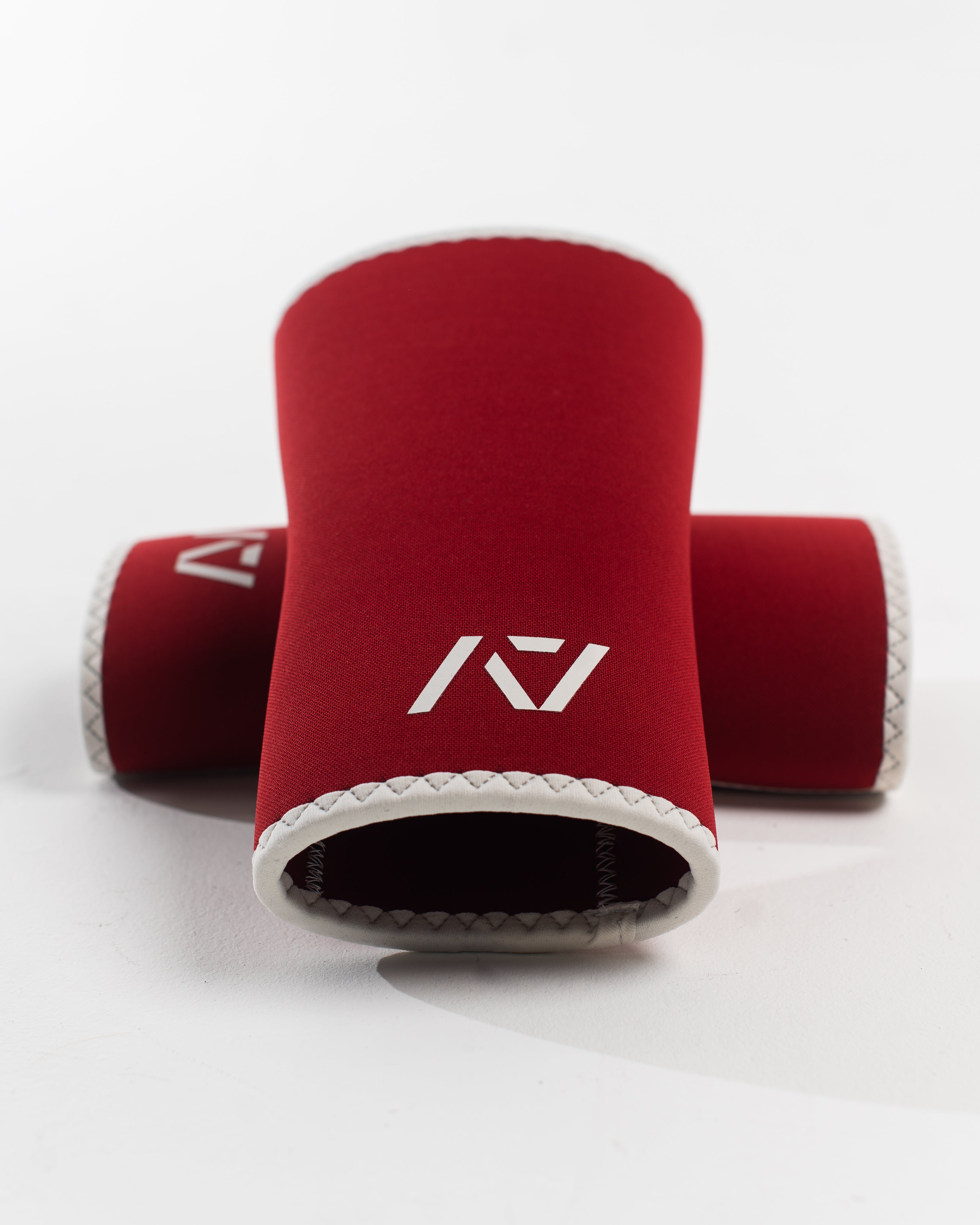 A pair of red knee sleeves with a white design that resembles a rose and tusk, symbolizing strength and beauty. The sleeves are designed with a hourglass-shaped center taper fit.