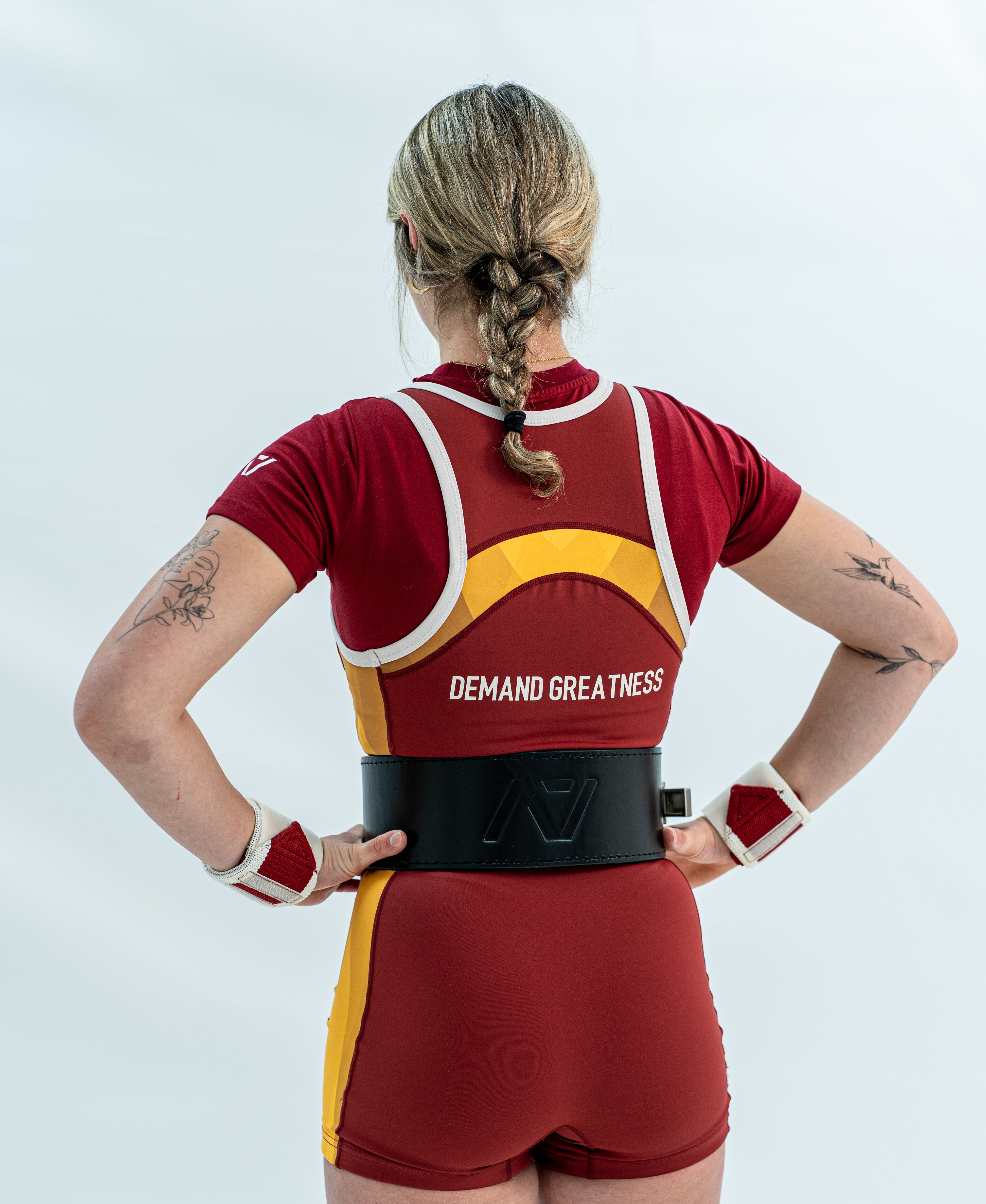 Person wearing a red and yellow rausch singlet with 'Demand Greatness' text on a white background