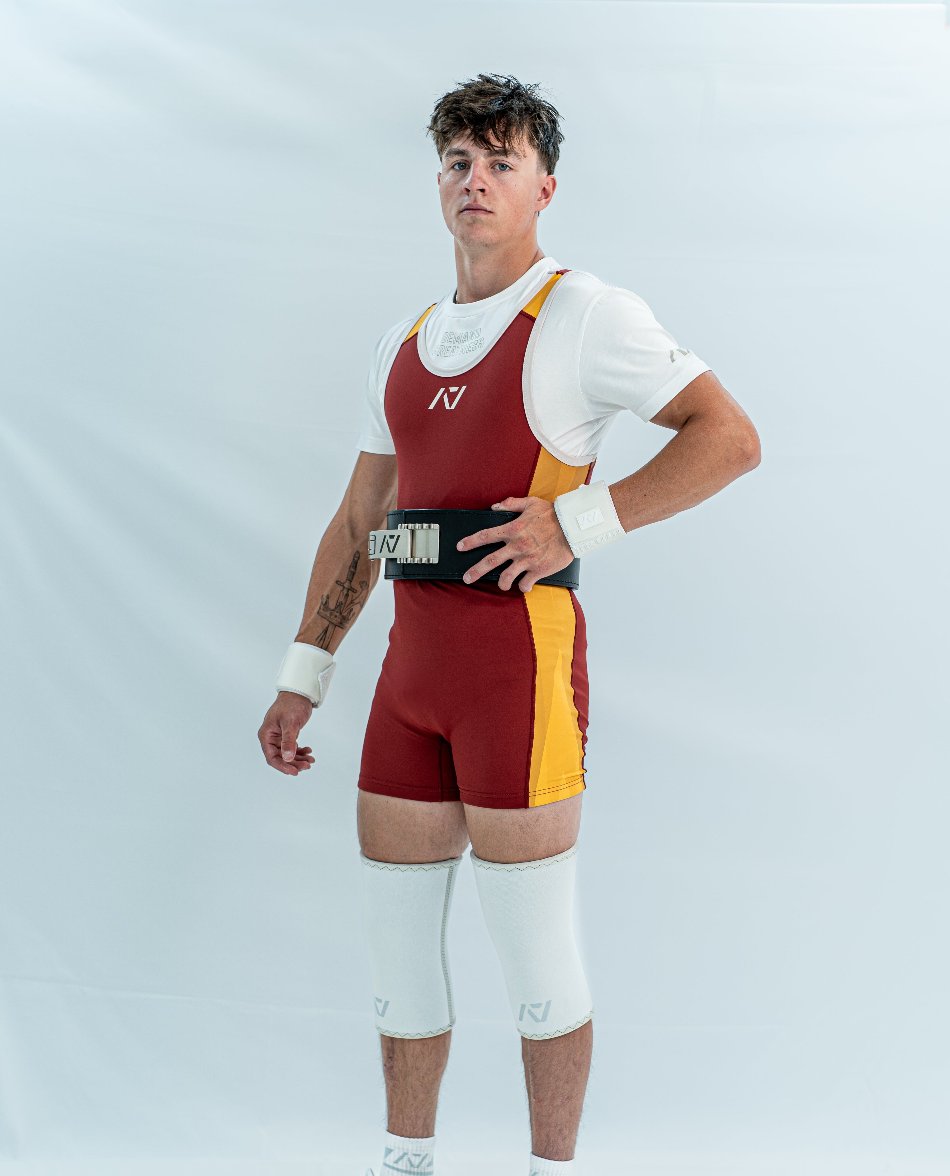 Male model wearing a maroon and yellow powerlifting singlet on a white background