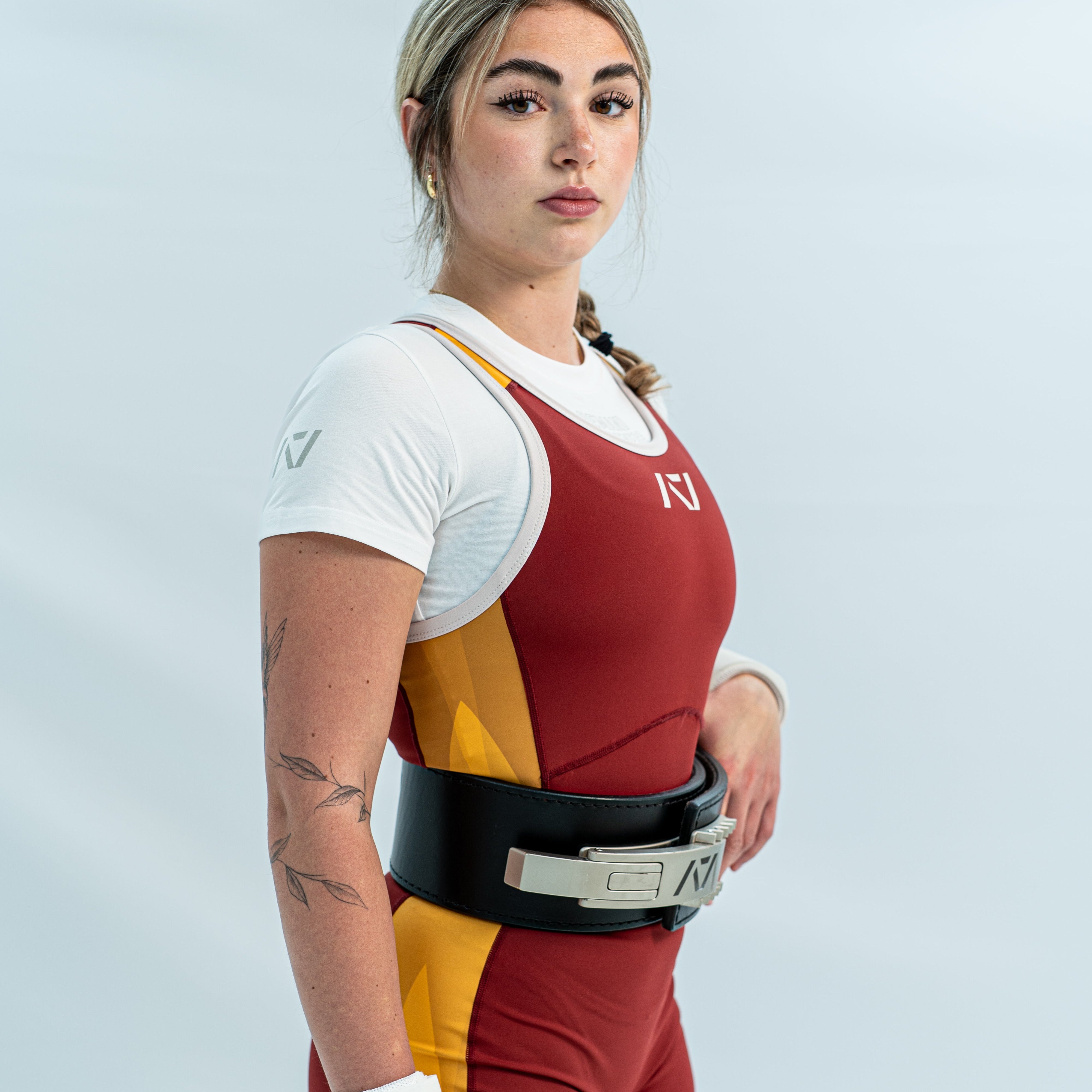 Female wearing a red and yellow rausch singlet with white accents on light gray background.