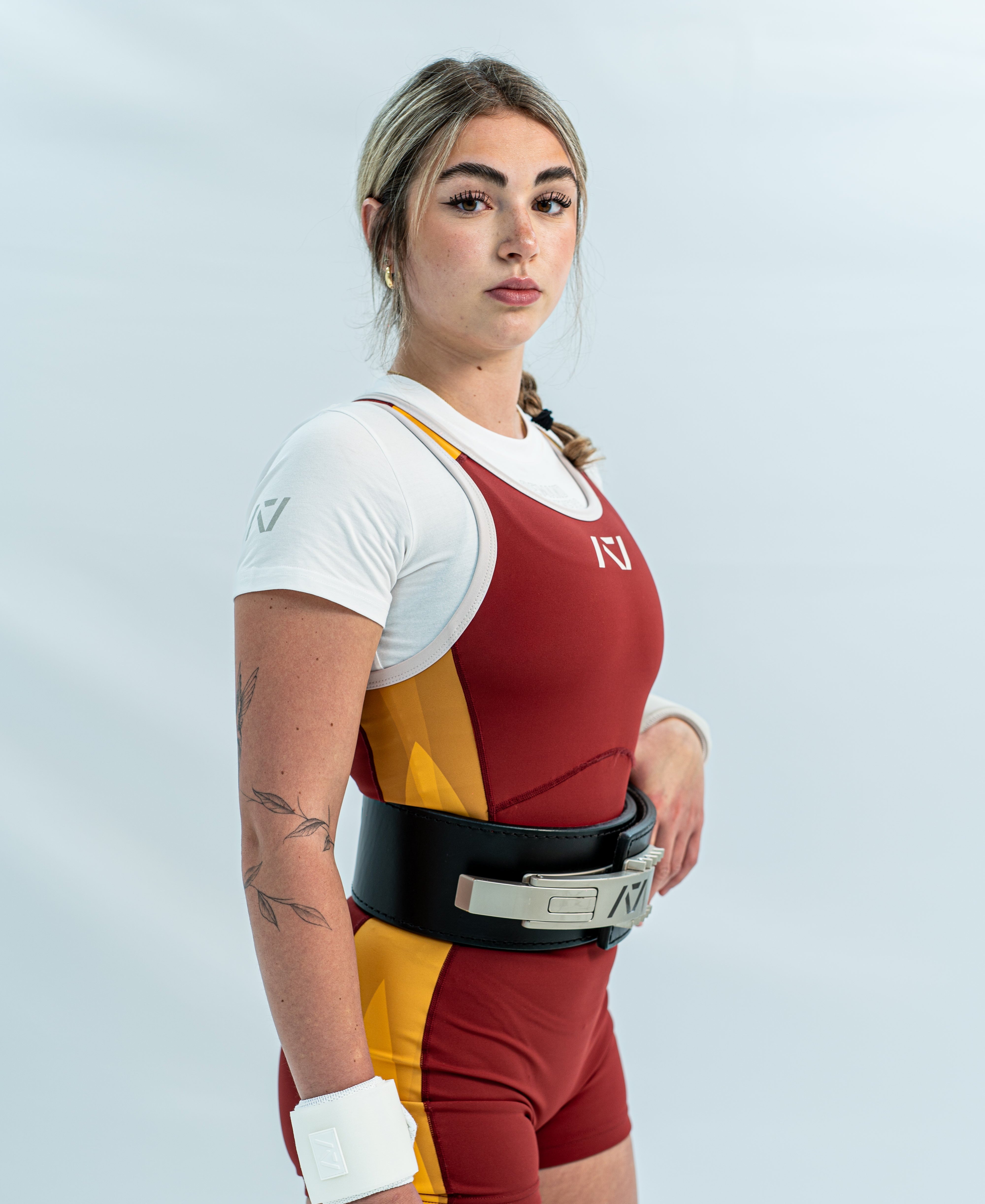 Female wearing a red and yellow rausch singlet with white accents on light gray background.
