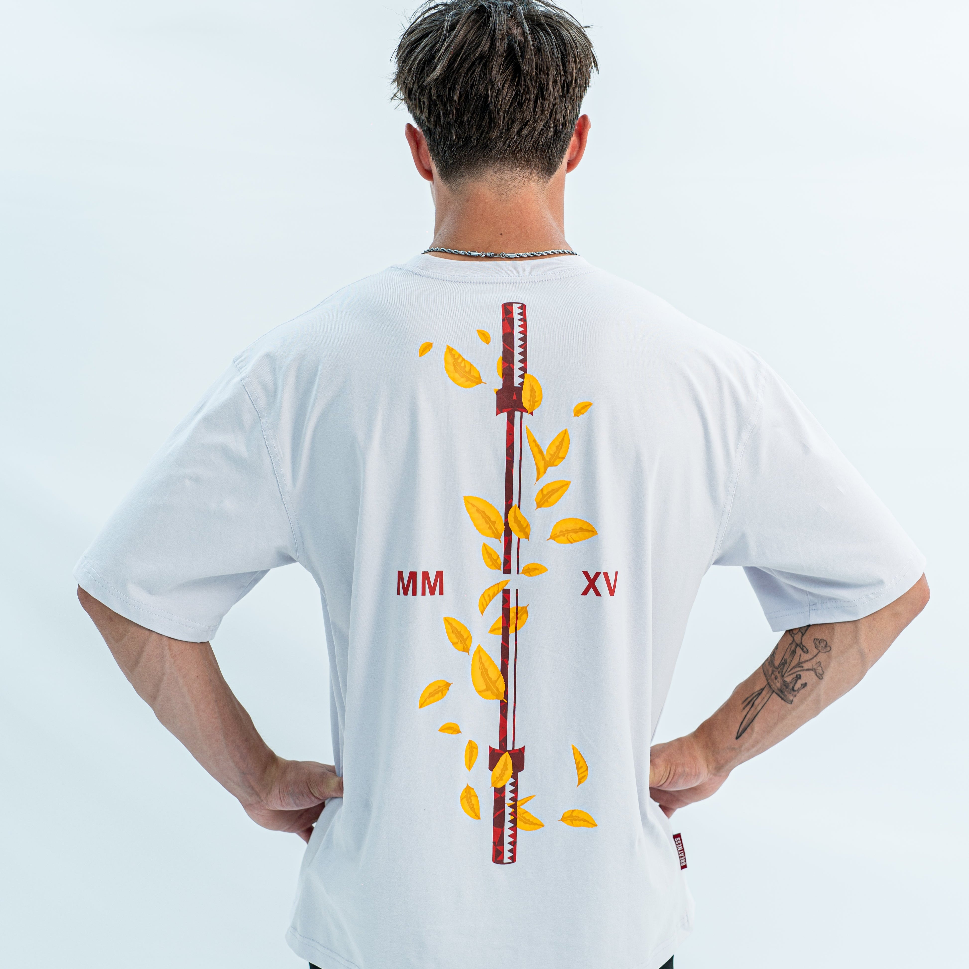 Male wearing a white over-fit shirt with a design on the back against a light gray background