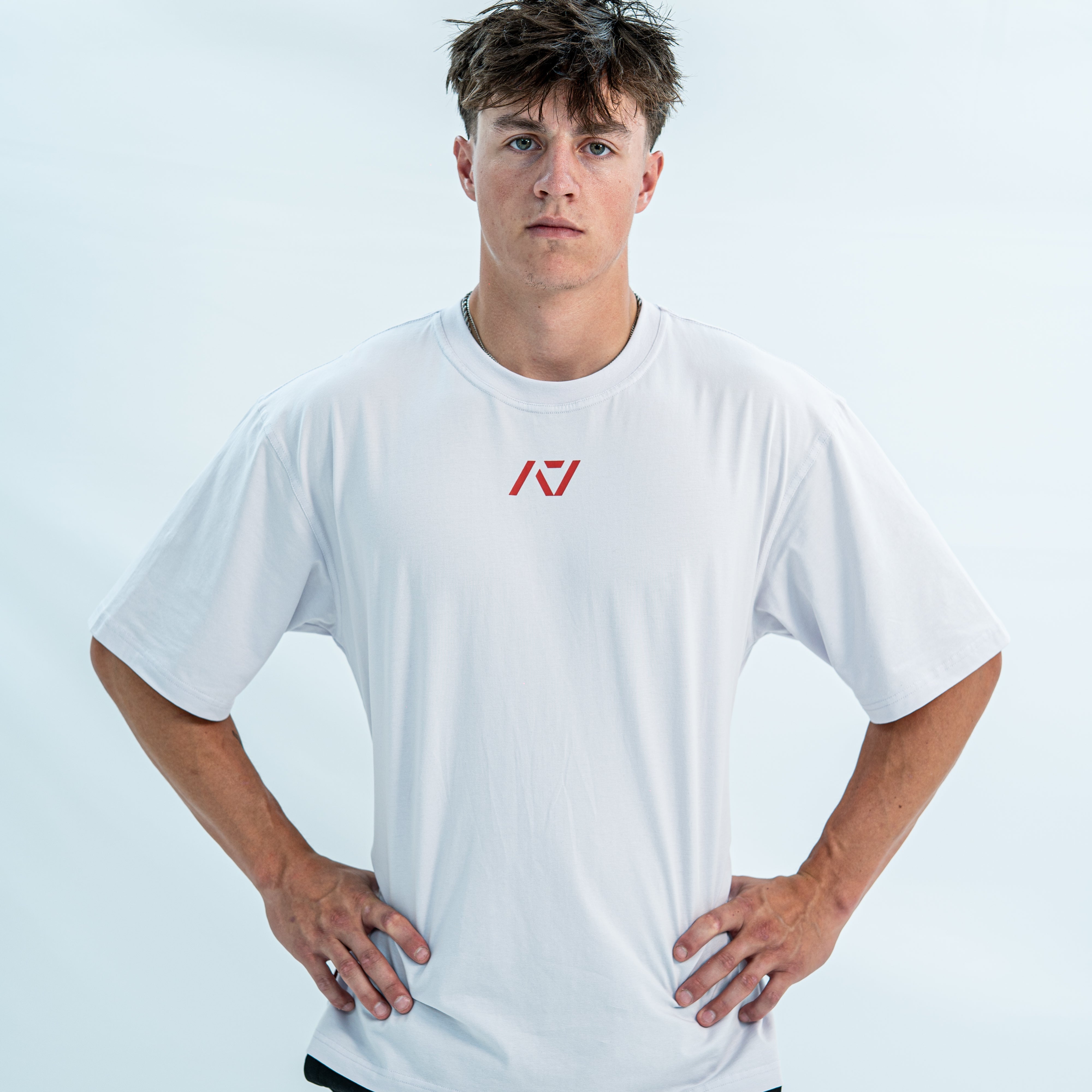 Male wearing a white over-fit shirt with a red logo on a light gray background