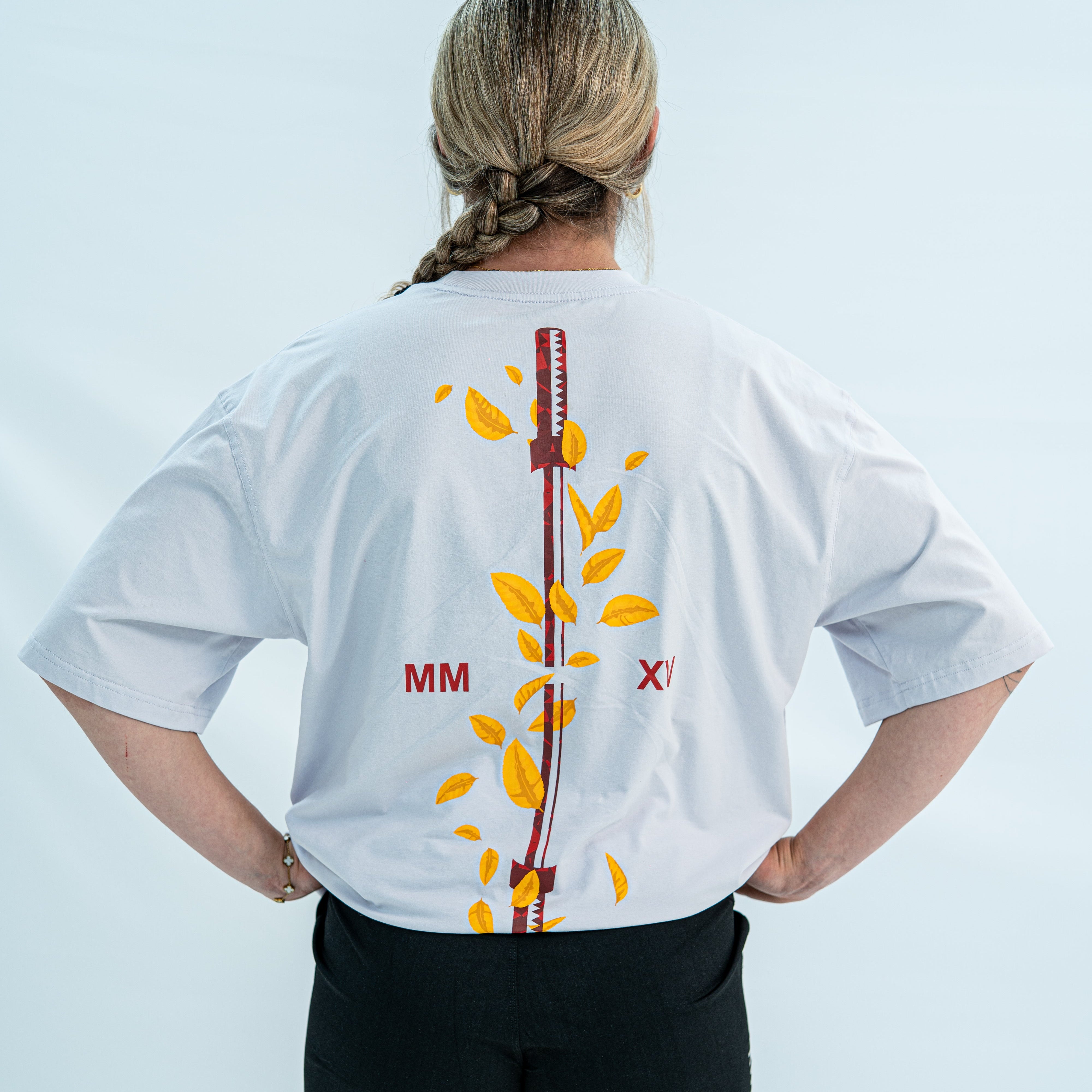 Female wearing a white over-fit shirt with a design on the back against a light gray background