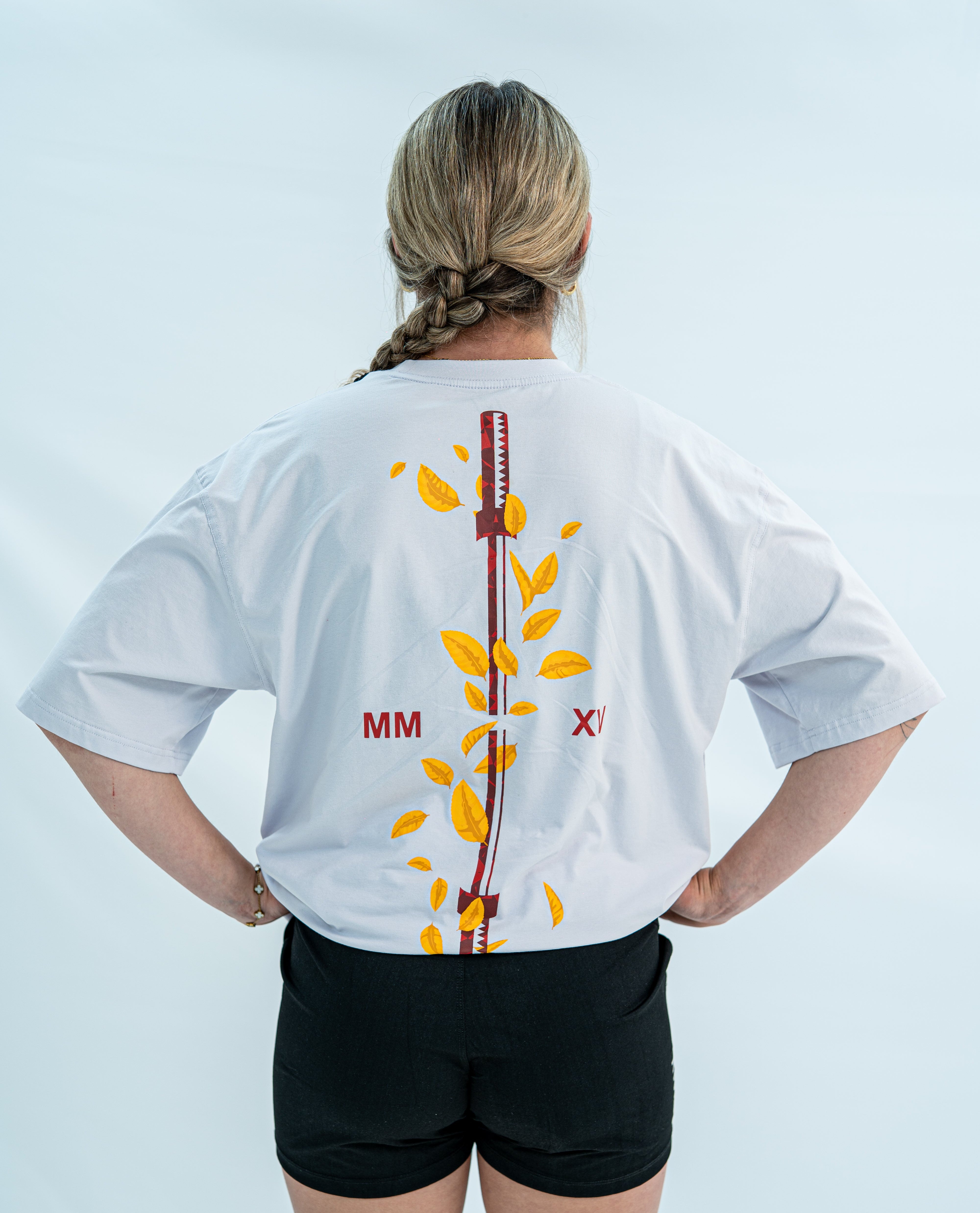 Female wearing a white over-fit shirt with a design on the back against a light gray background