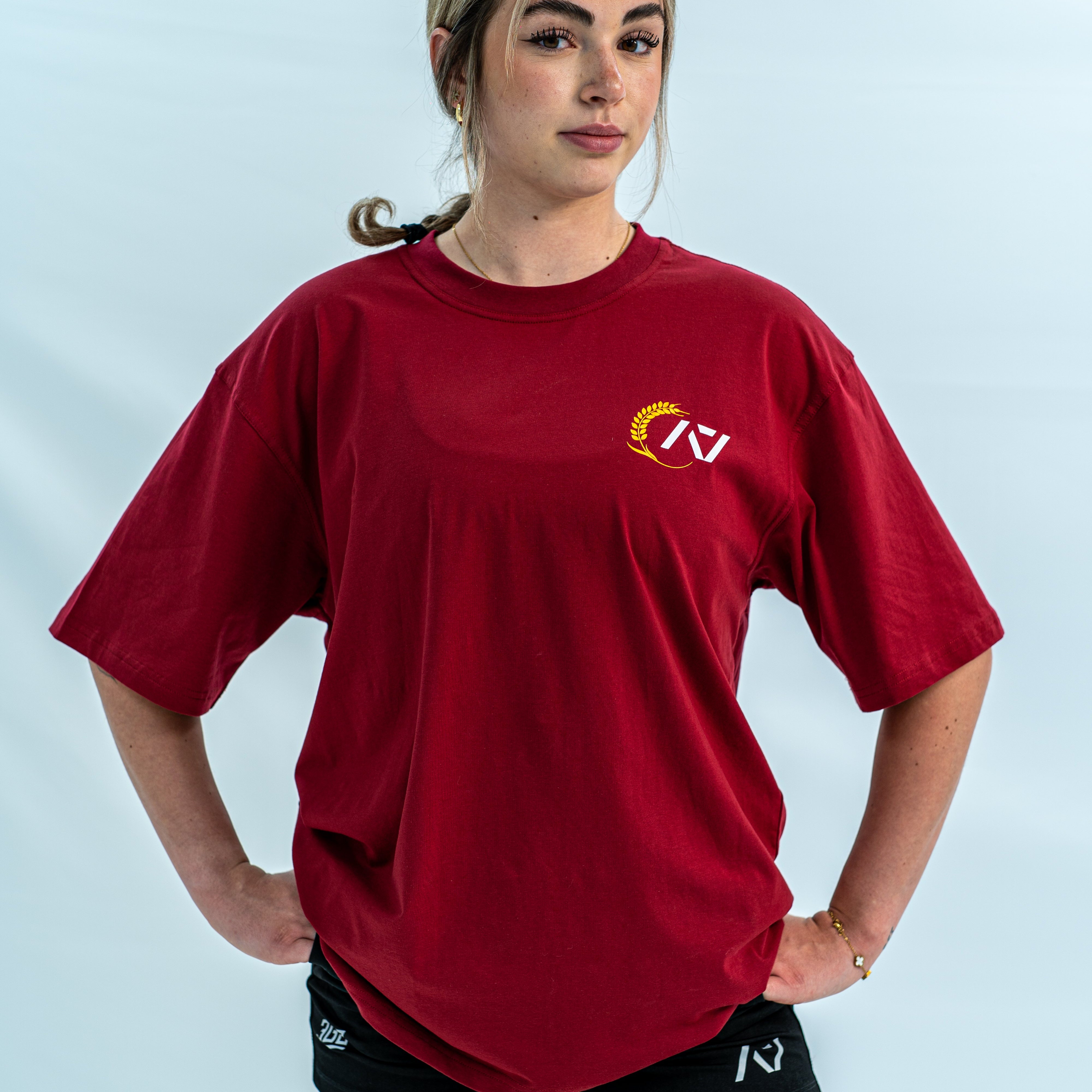 Female wearing a red over-fit shirt with a logo on a light gray background