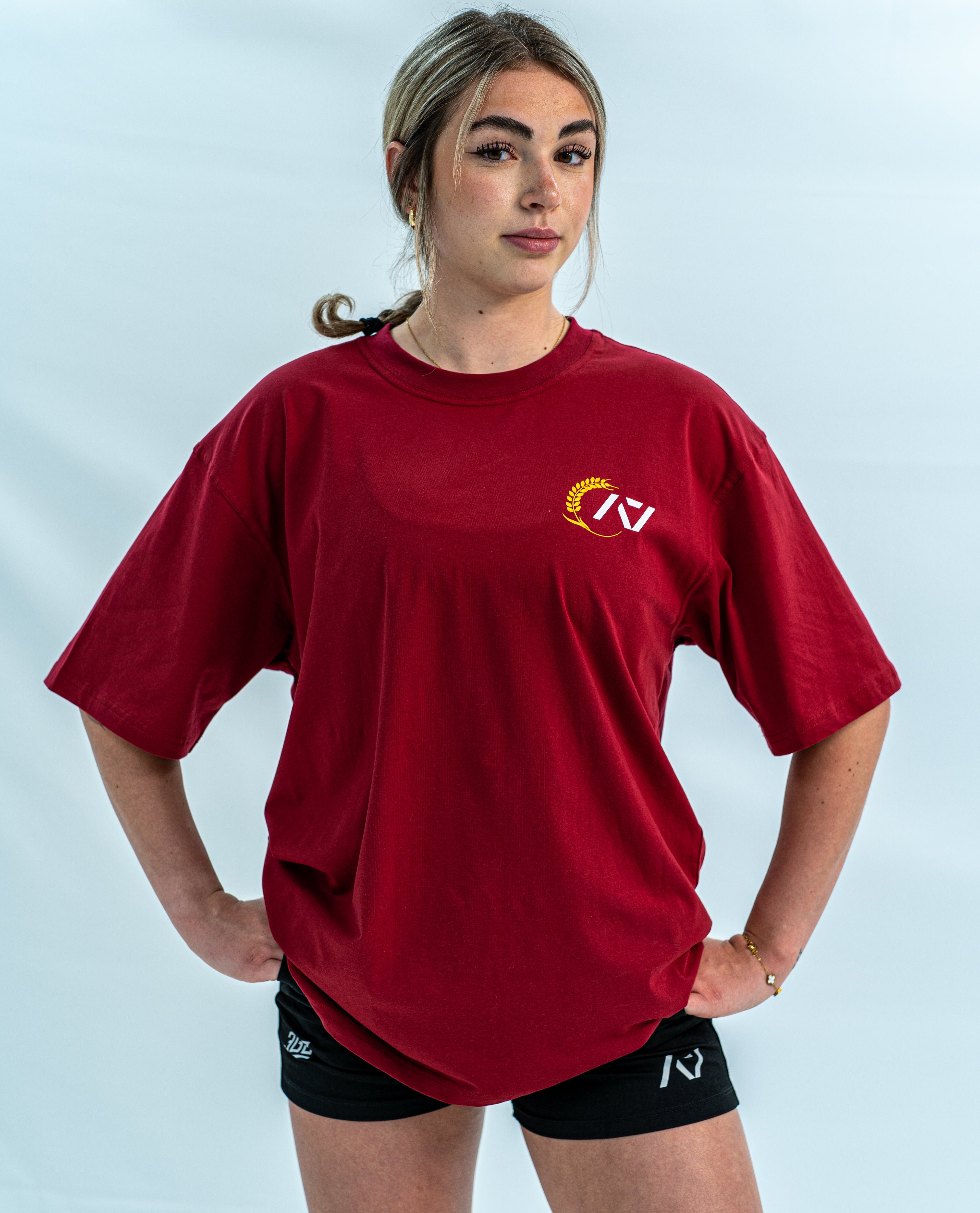 Female wearing a red over-fit shirt with a logo on a light gray background
