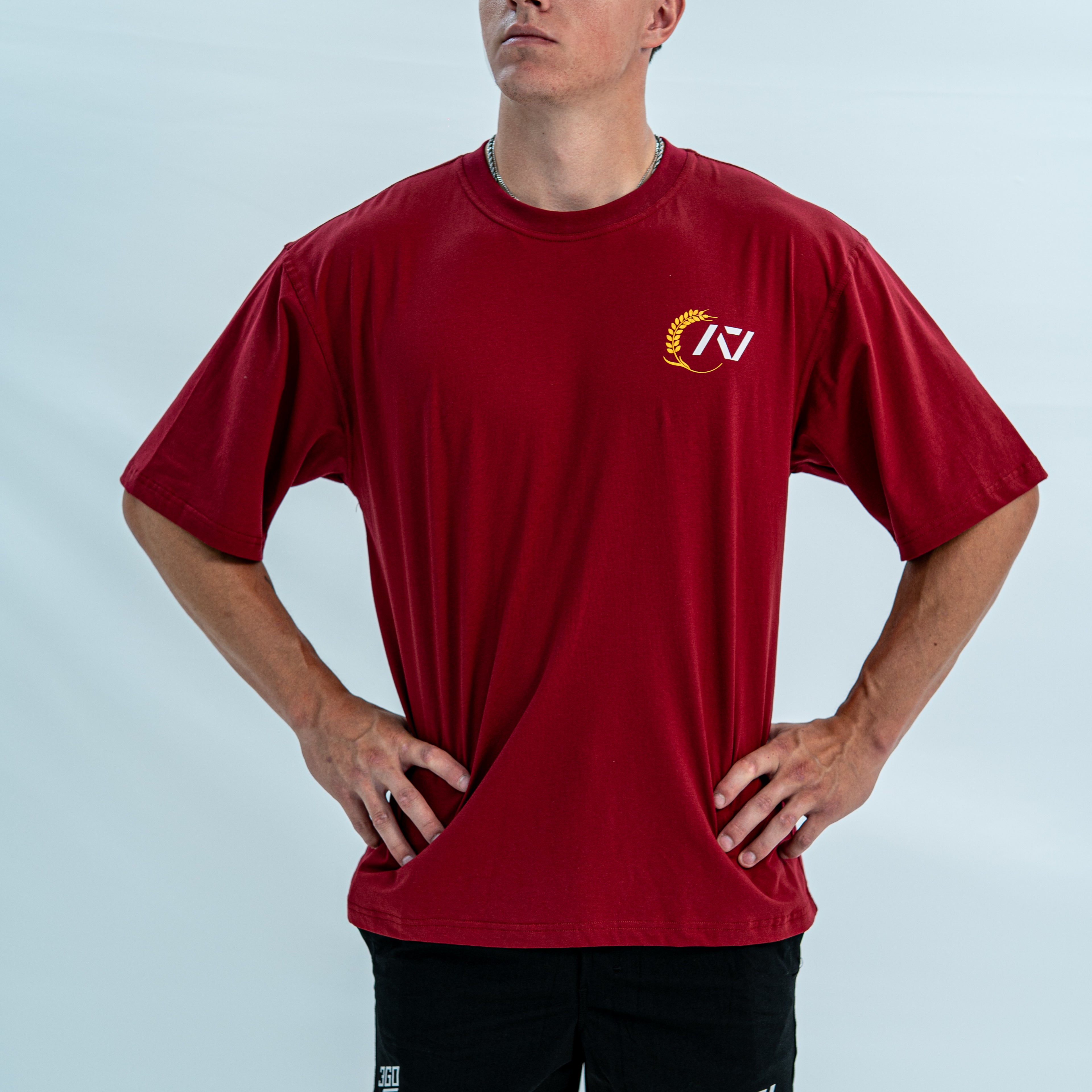 Male wearing a red over-fit unisex shirt with a logo on a light gray background