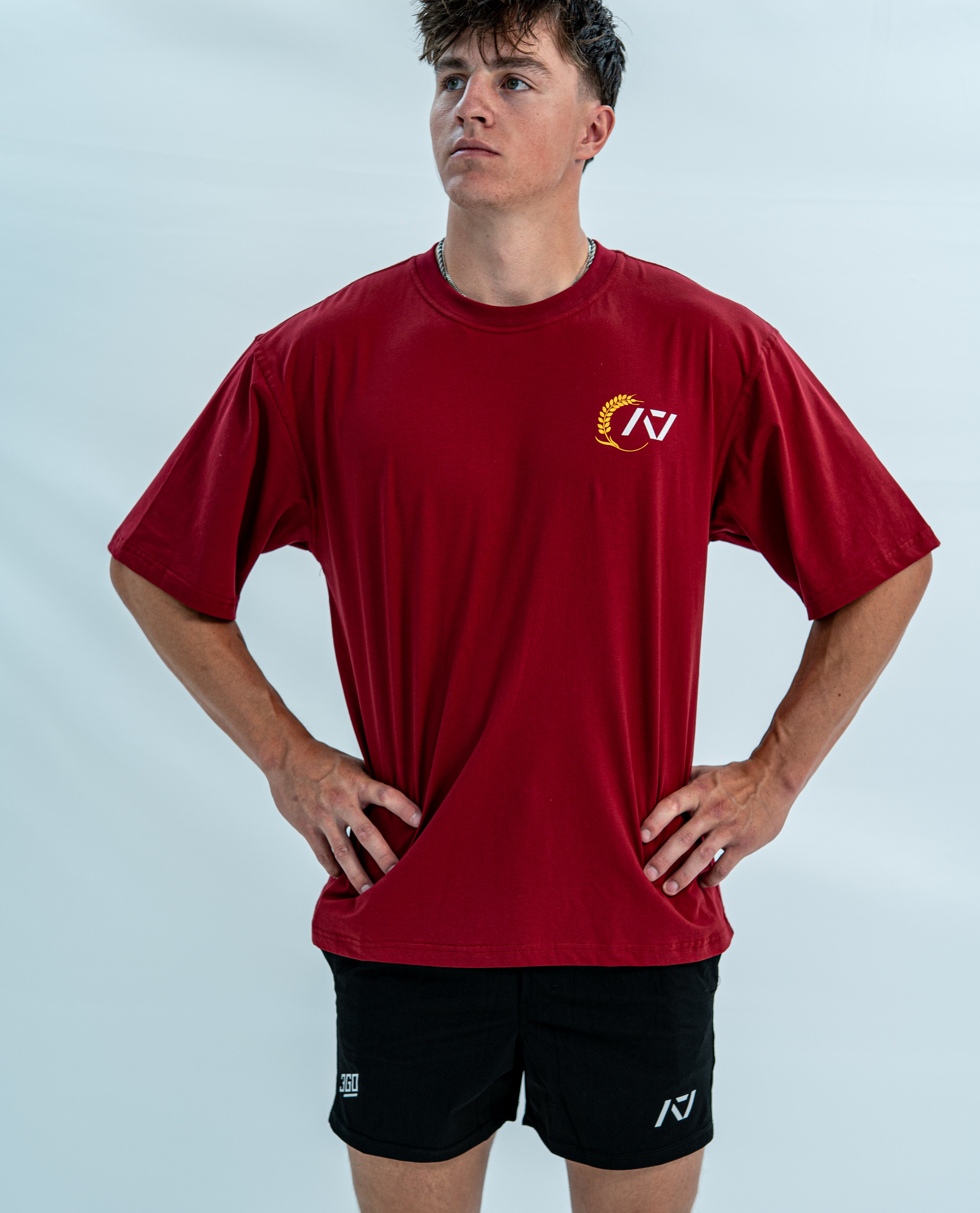 Male wearing a red over-fit unisex shirt with a logo on a light gray background