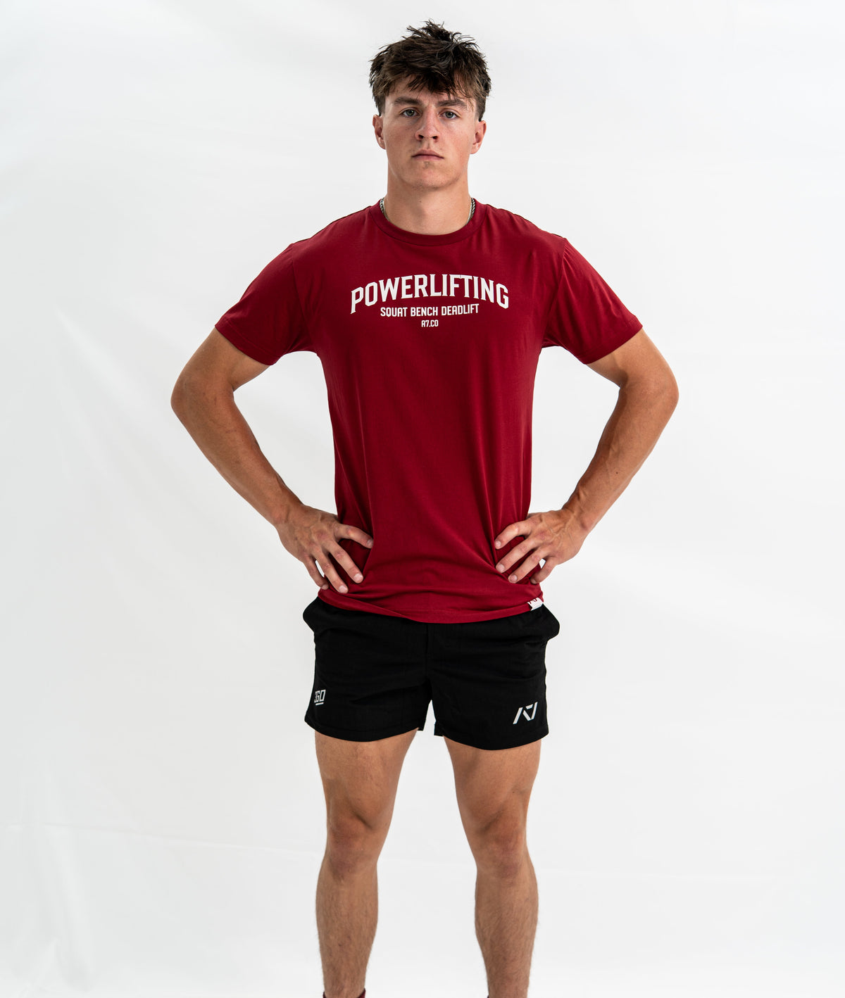 Person wearing a red 'Powerlifting' Bar Grip Shirt and black shorts on a white background
