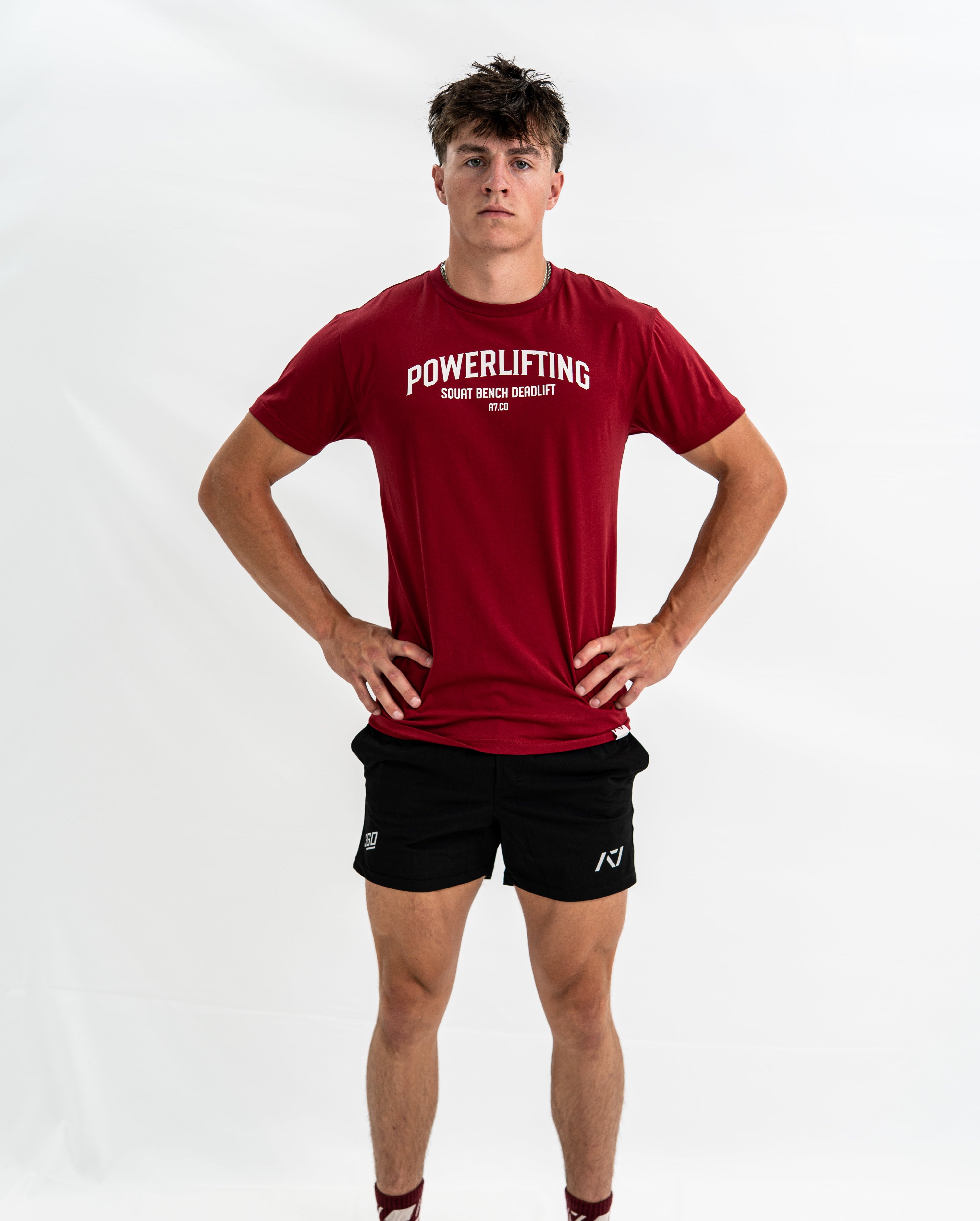 Person wearing a red 'Powerlifting' Bar Grip Shirt and black shorts on a white background