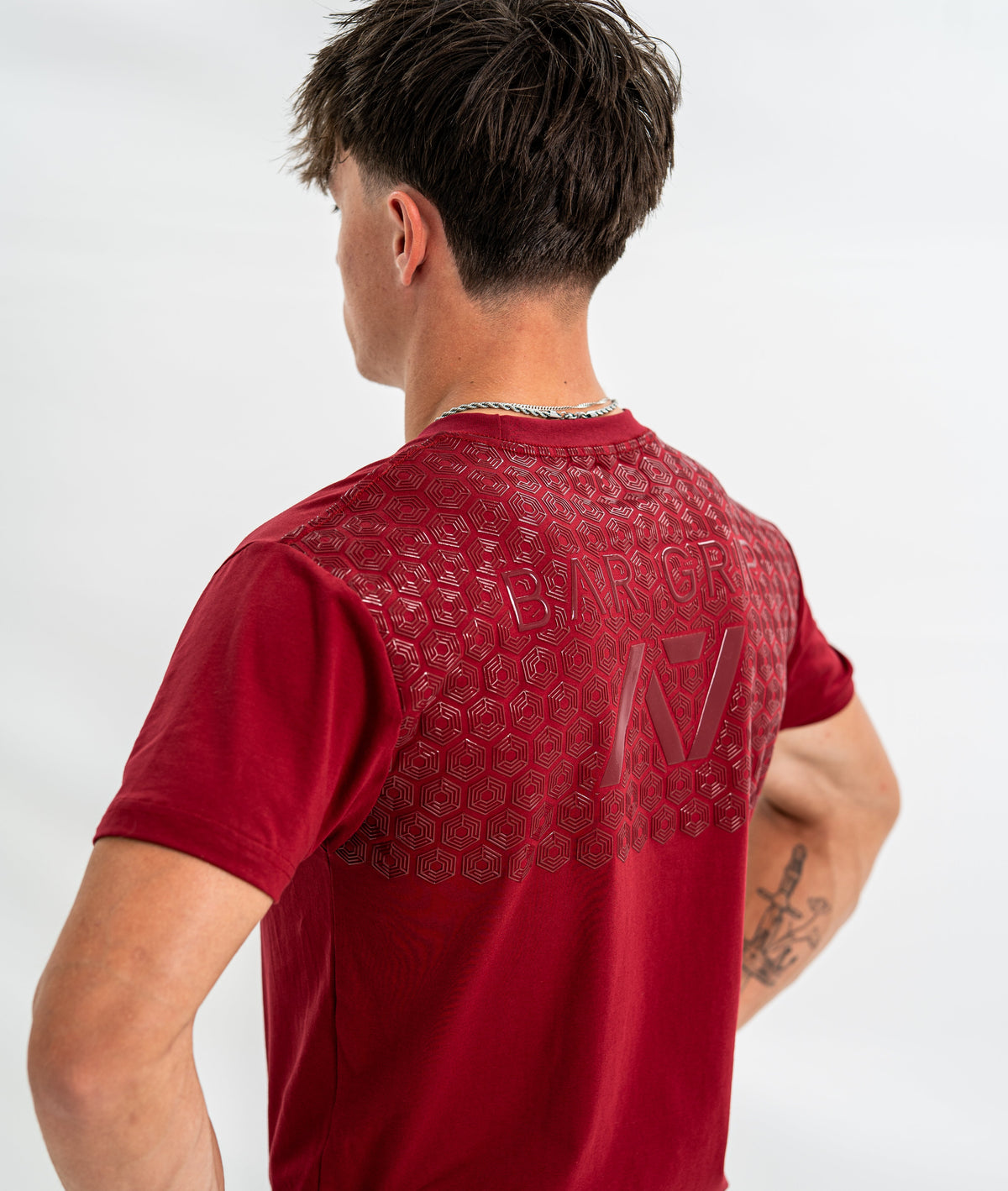Male wearing a red bar grip shirt with a brand logo on the back against a white background