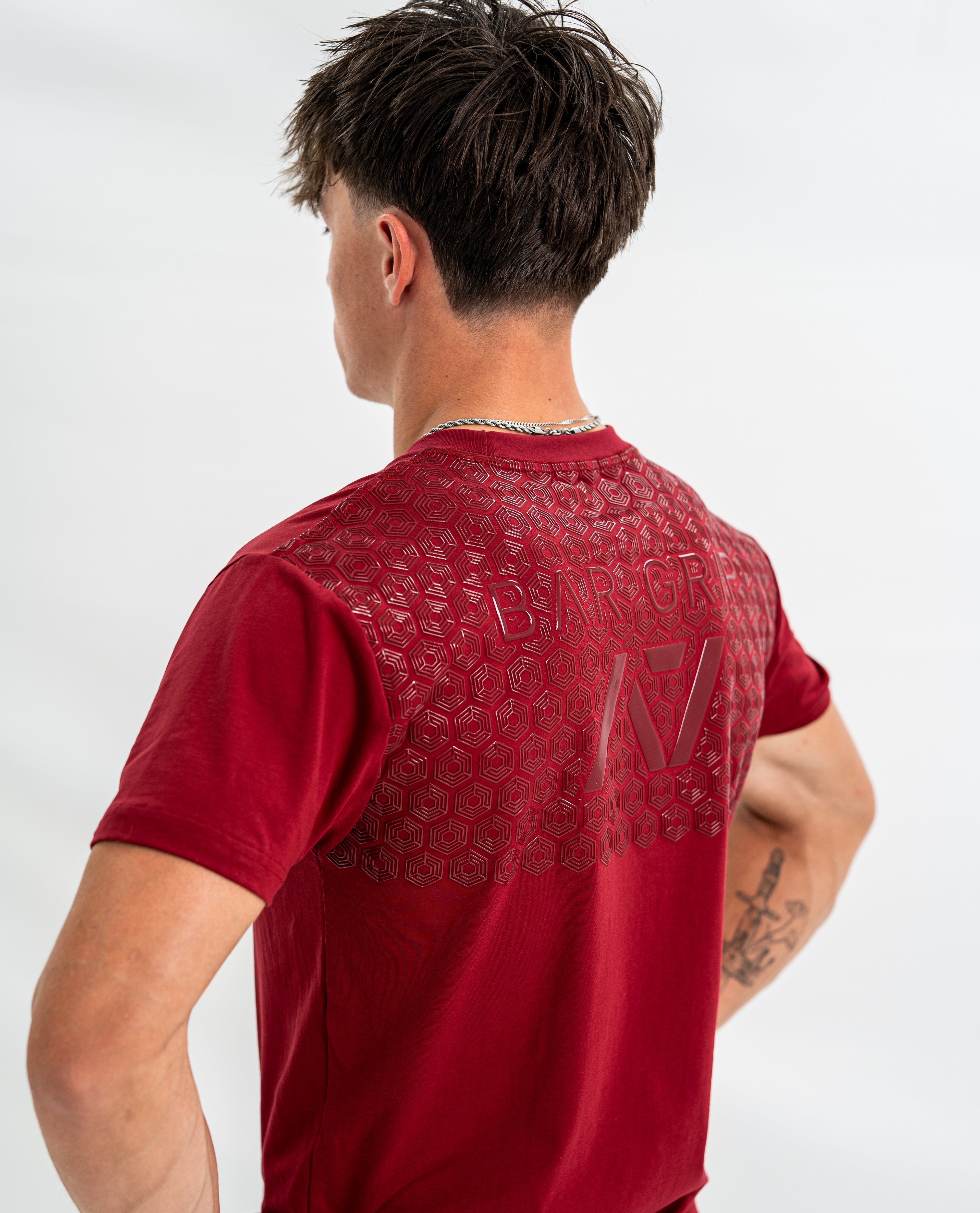 Male wearing a red bar grip shirt with a brand logo on the back against a white background