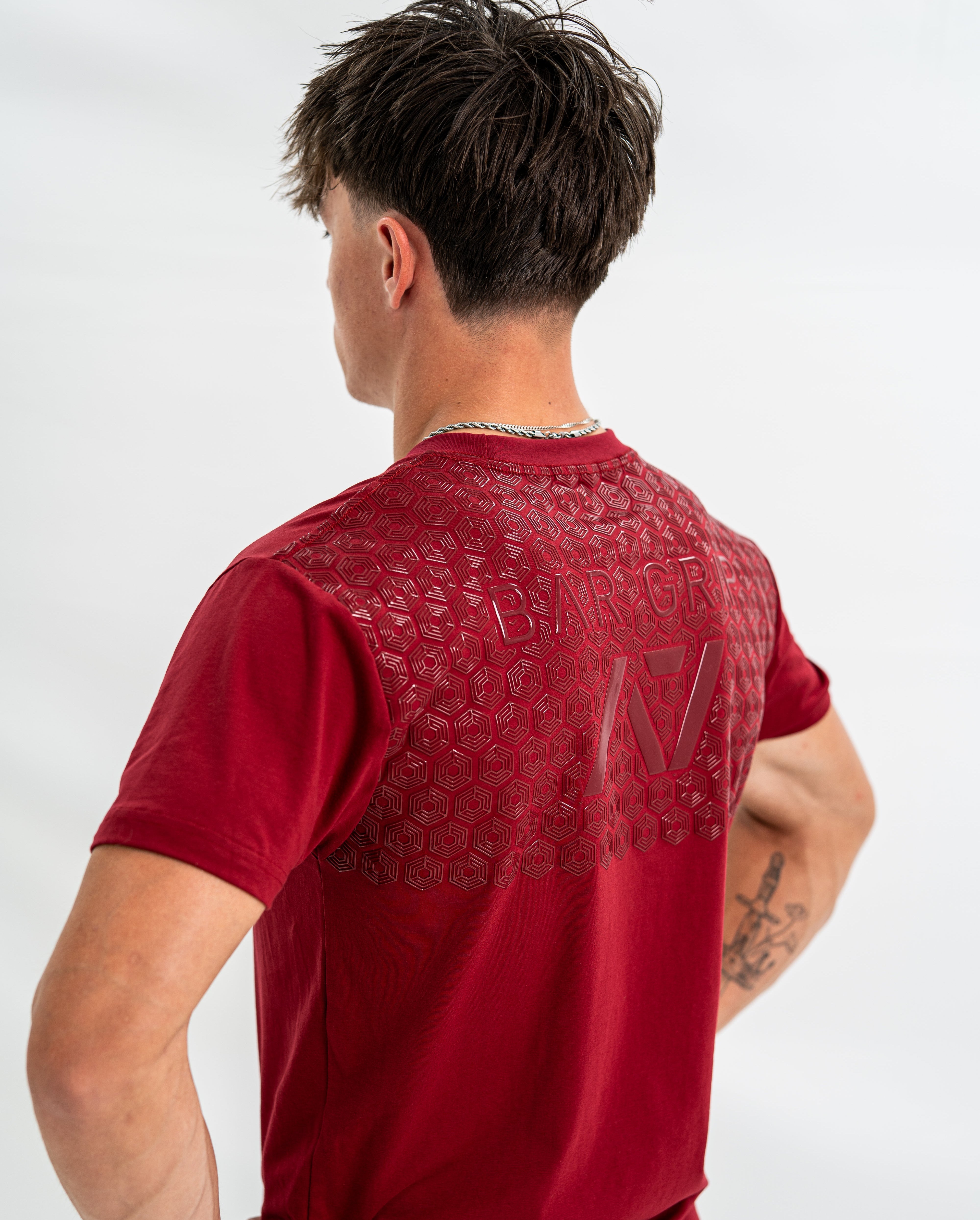 Male wearing a red bar grip shirt with a brand logo on the back against a white background