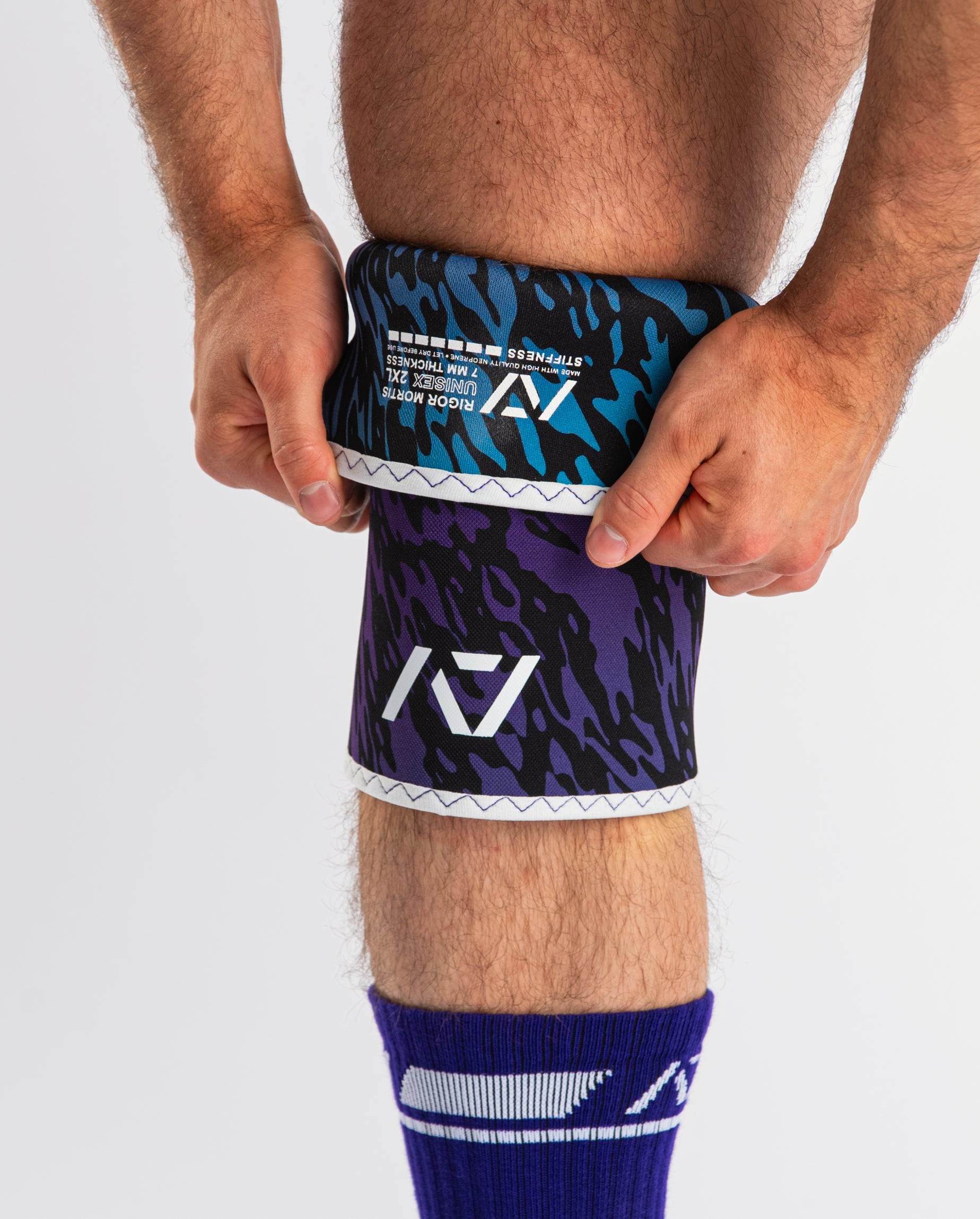 Front view of A7 Hourglass Knee Sleeves – Rigor Mortis – Violet Tiger on lifter's knees, highlighting label and the lifter putting the sleeve on.