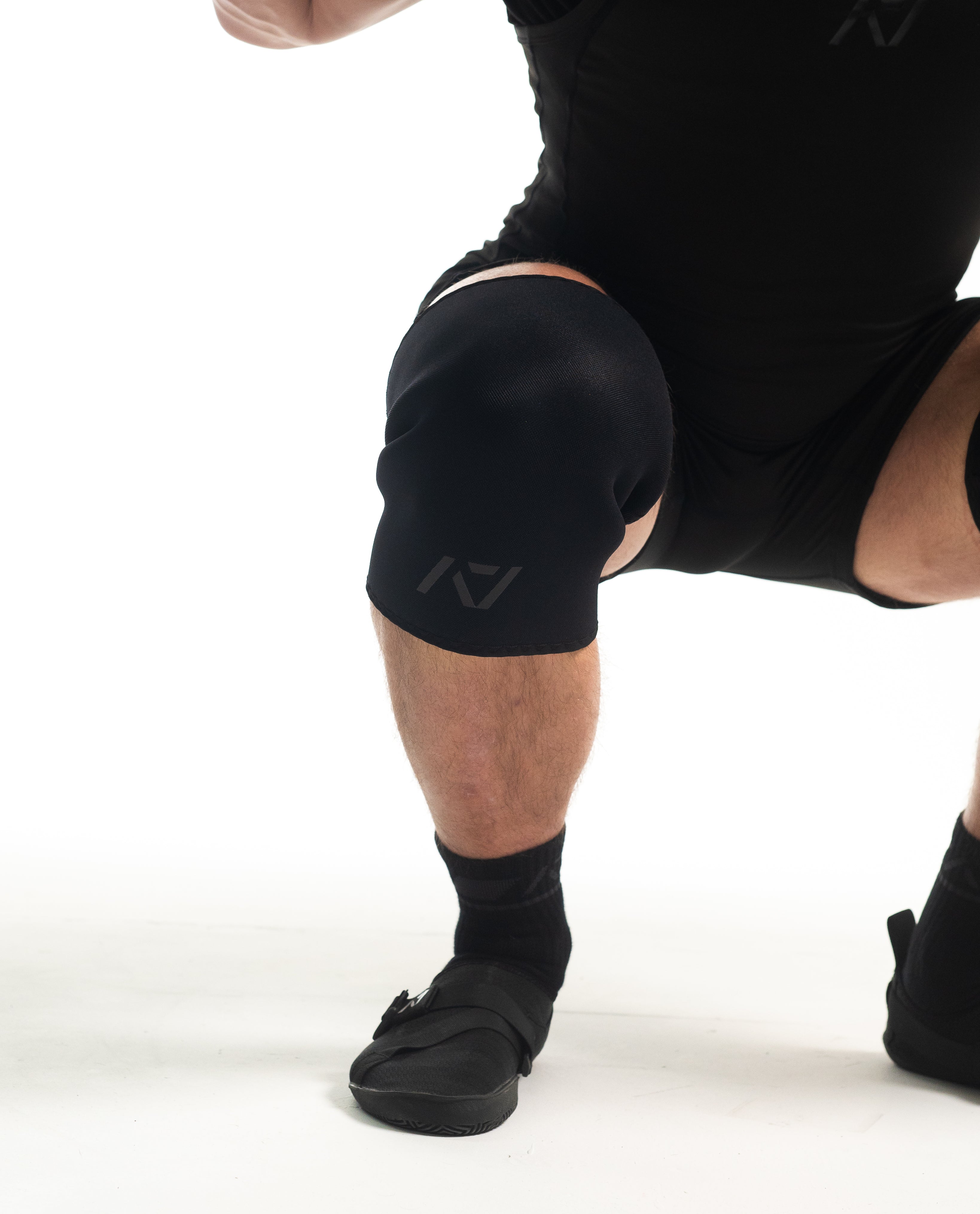 Athlete wearing A7 Hourglass Knee Sleeves – Stealth during a squat, showcasing ergonomic hourglass design for optimal knee compression.