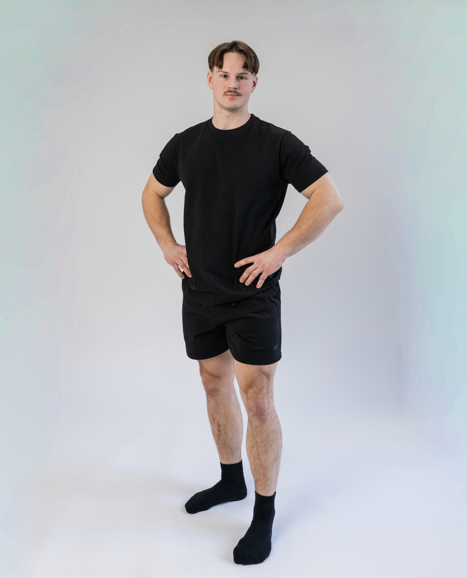 Man wearing a black t-shirt, shorts, and socks on a white background