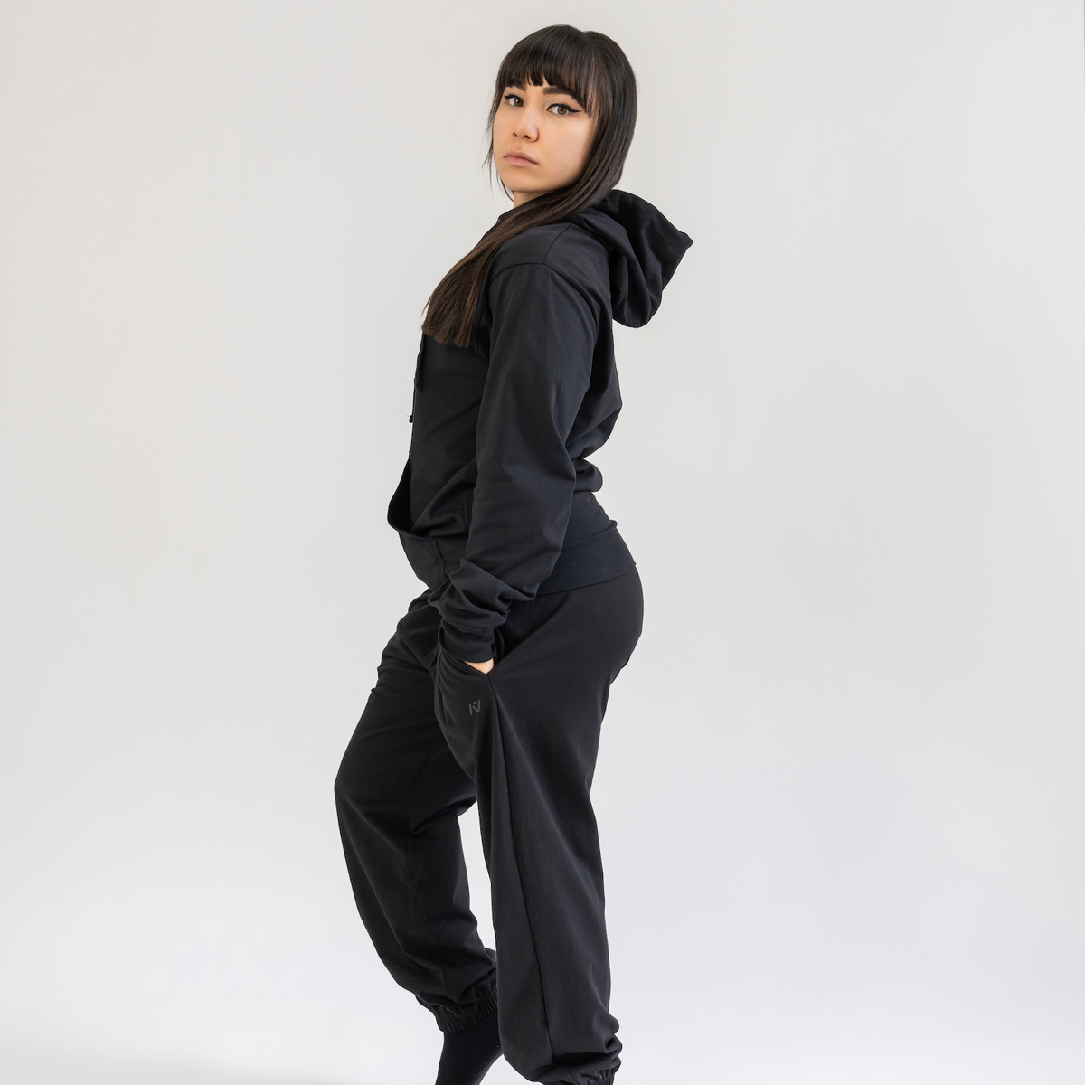 Person wearing a black hoodie and pants on a white background