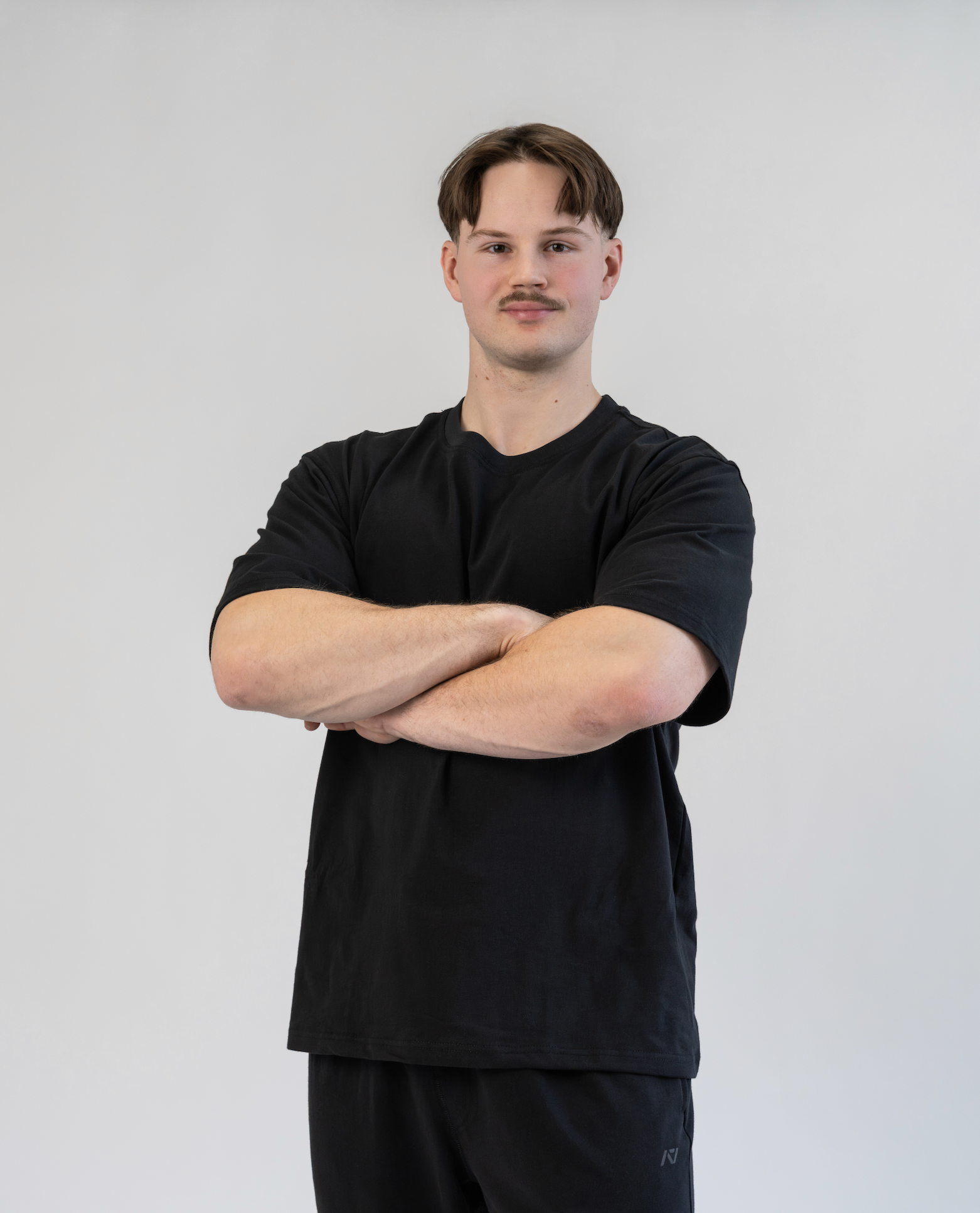 Man wearing a black t-shirt and dark pants against a plain background