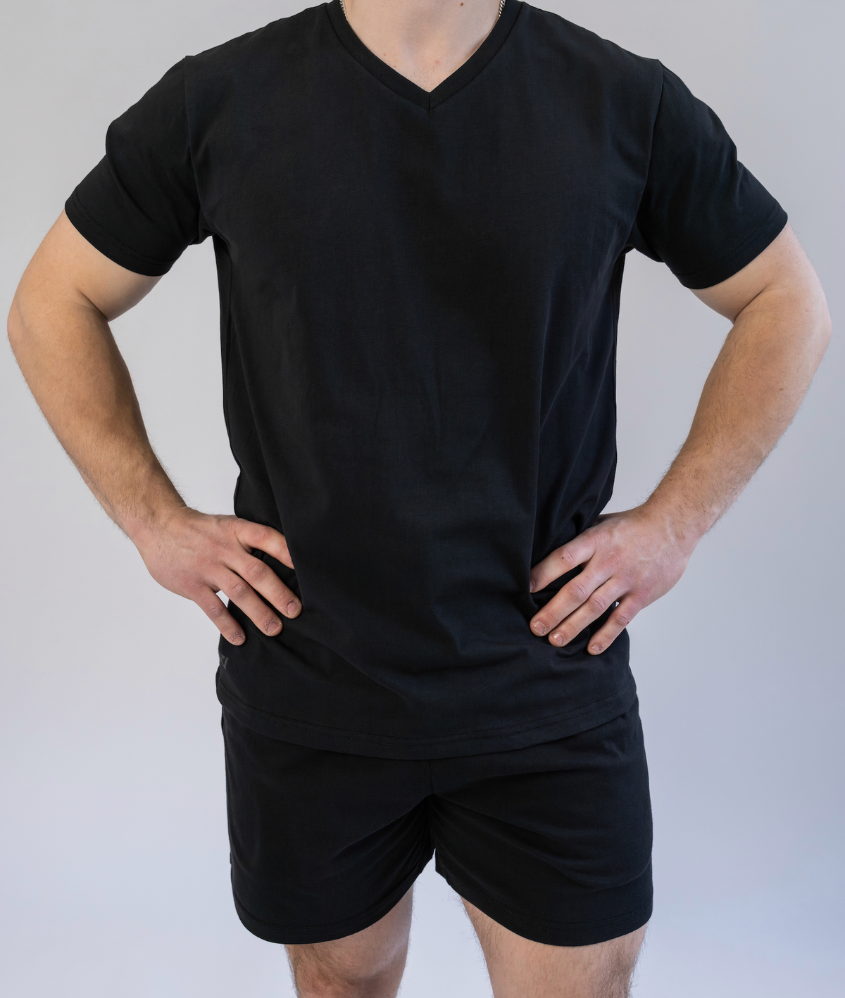 Person wearing a black V-neck t-shirt and black shorts on a plain background