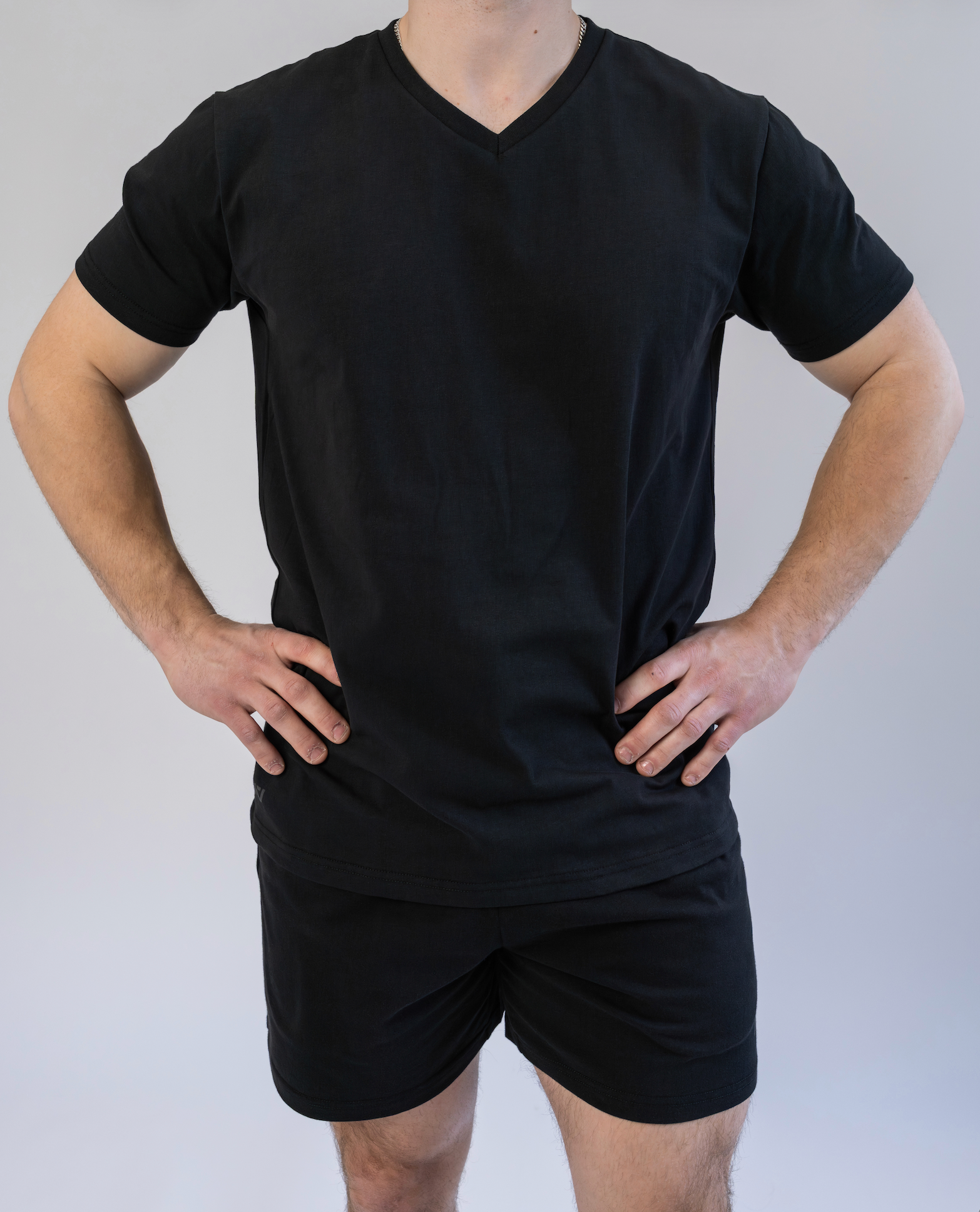 Person wearing a black V-neck t-shirt and black shorts on a plain background