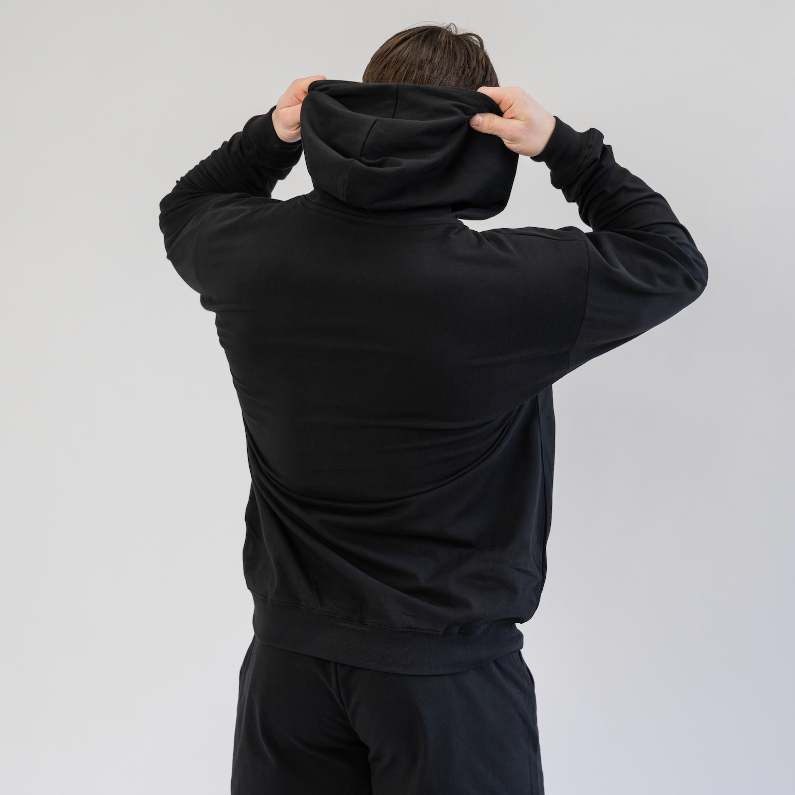 Person wearing a black hoodie and shorts set against a plain background