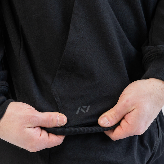 Person wearing a black hoodie with a logo on the chest pocket against a light gray background