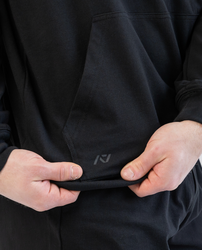 Person wearing a black hoodie with a logo on the chest pocket against a light gray background