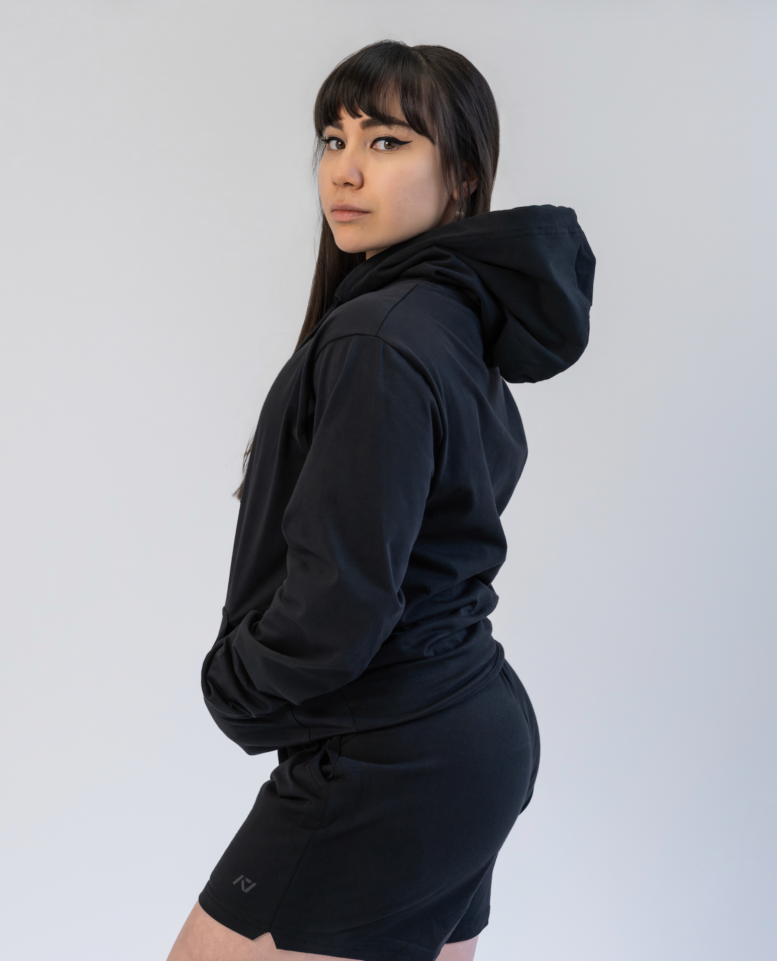Person wearing a black hoodie and shorts on a white background