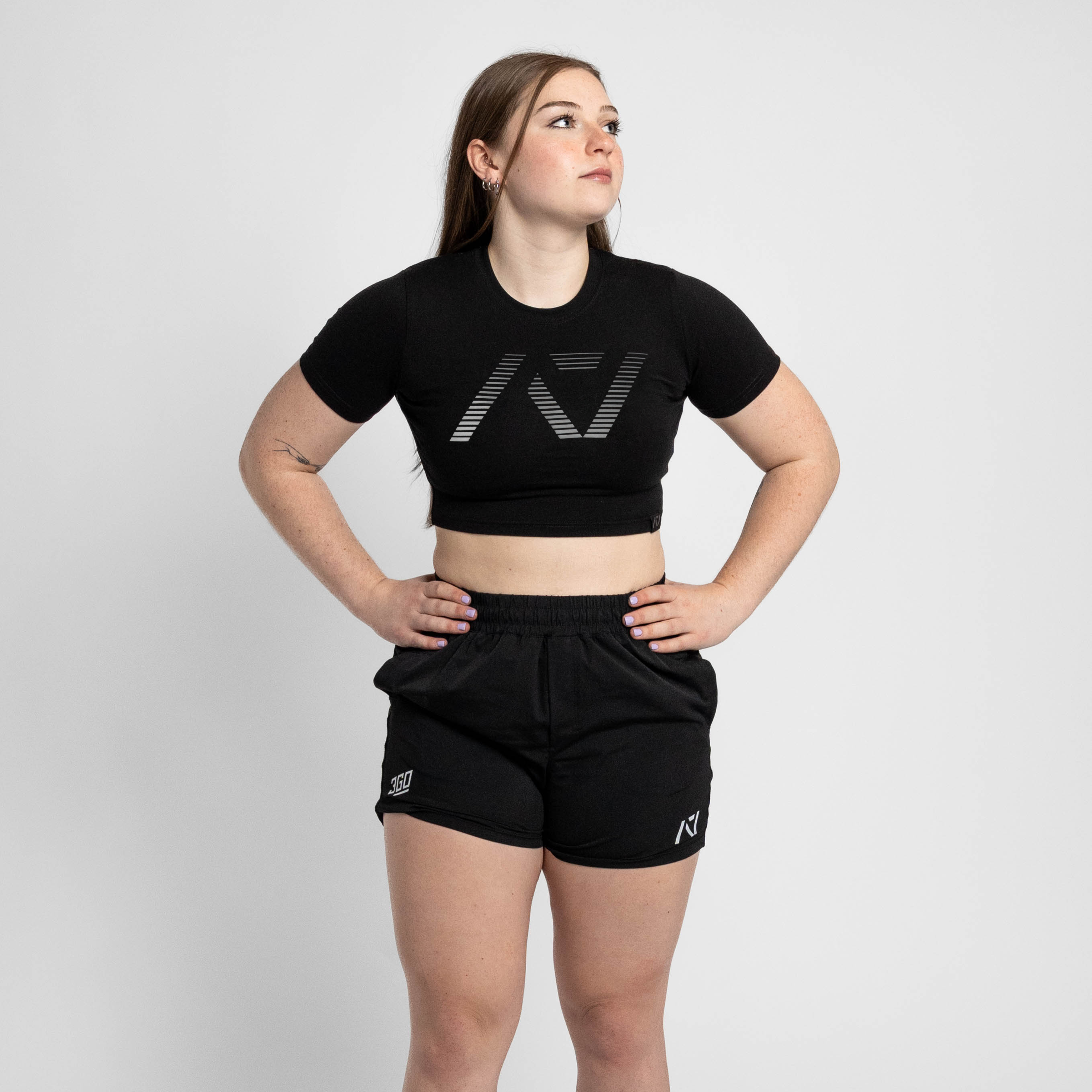 Woman wearing a black crop top and shorts with a logo on a white background