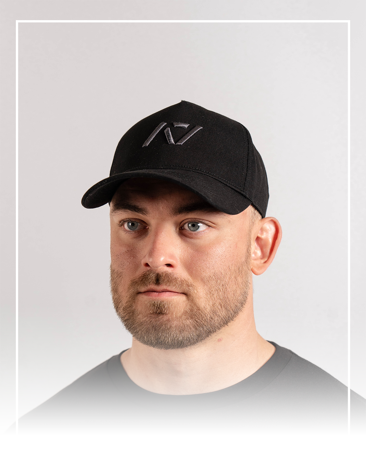 Man wearing a black cap with a logo on a light gray background