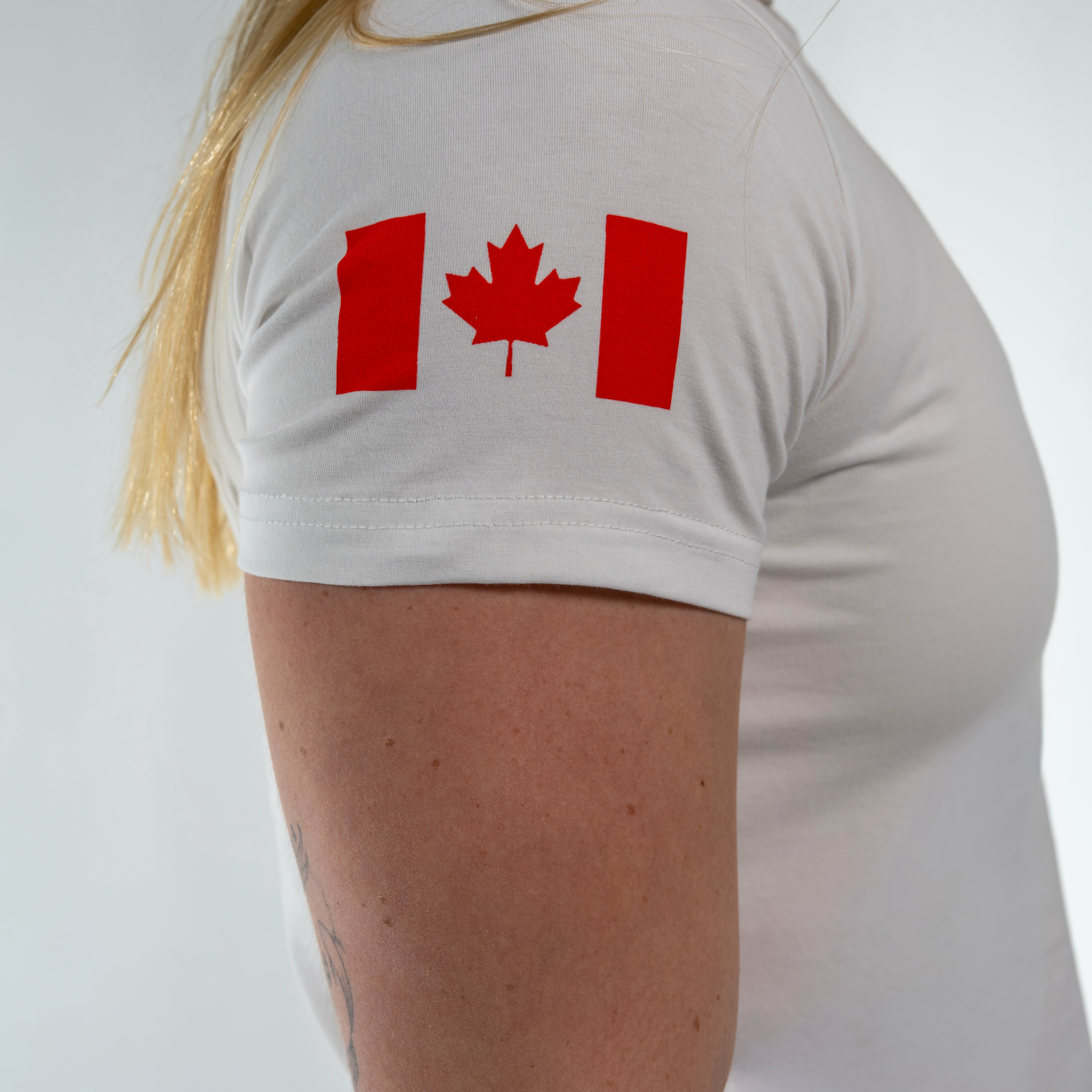 Person wearing a white t-shirt with a red maple leaf design on a plain background