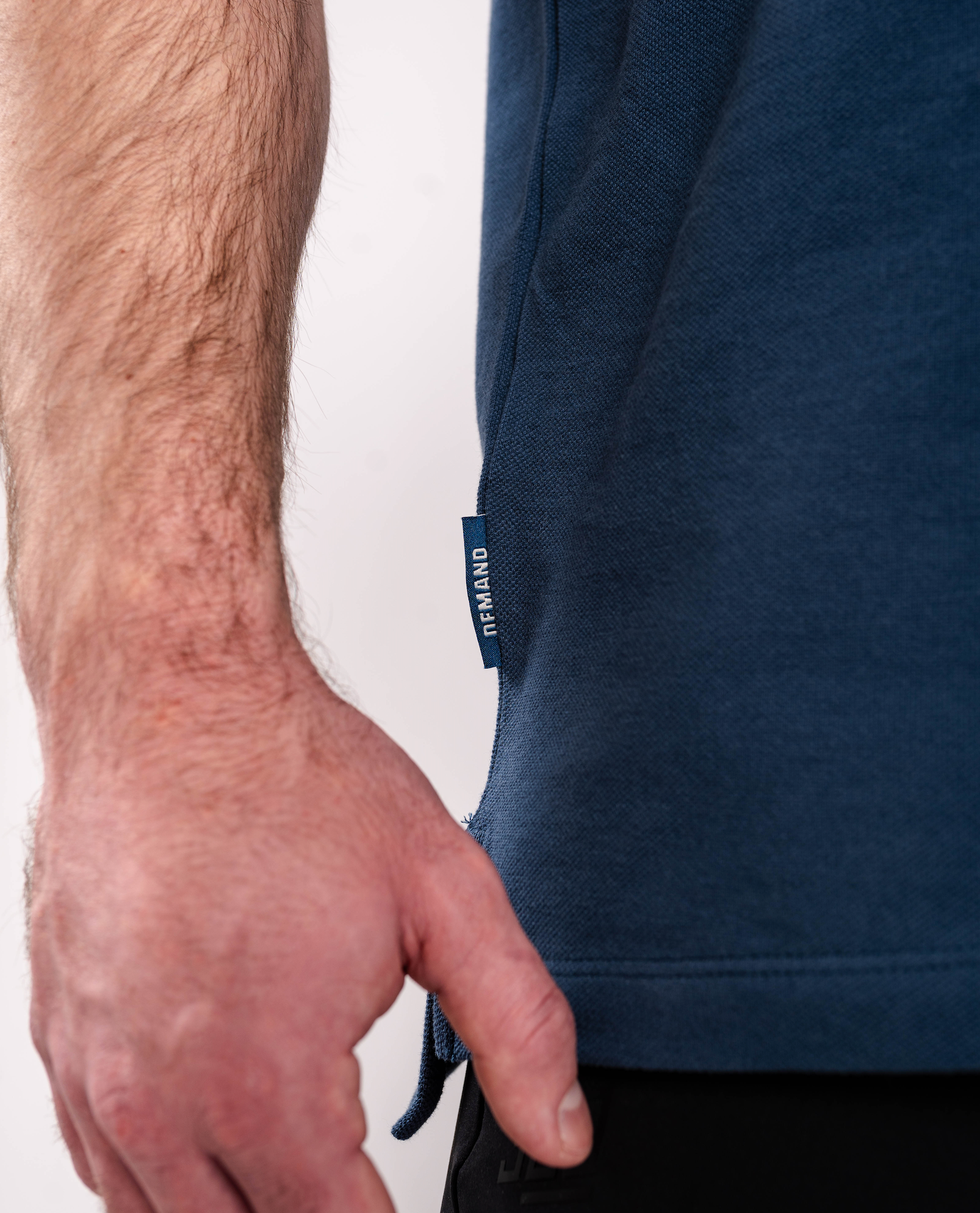 Close-up of the woven A7 hem tag on the Cotton Polo – Tides, stitched at the bottom hem for a subtle branded detail.