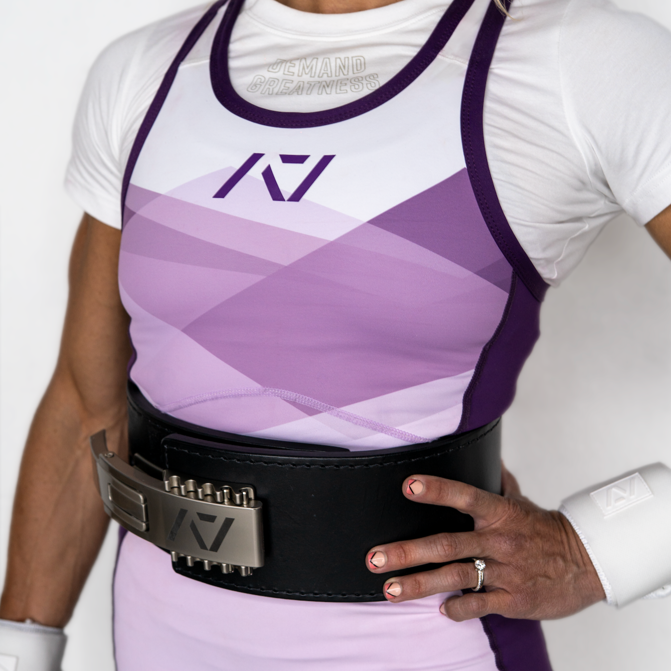 Person wearing a white and purple IPF Approved singlet with a belt on a plain background