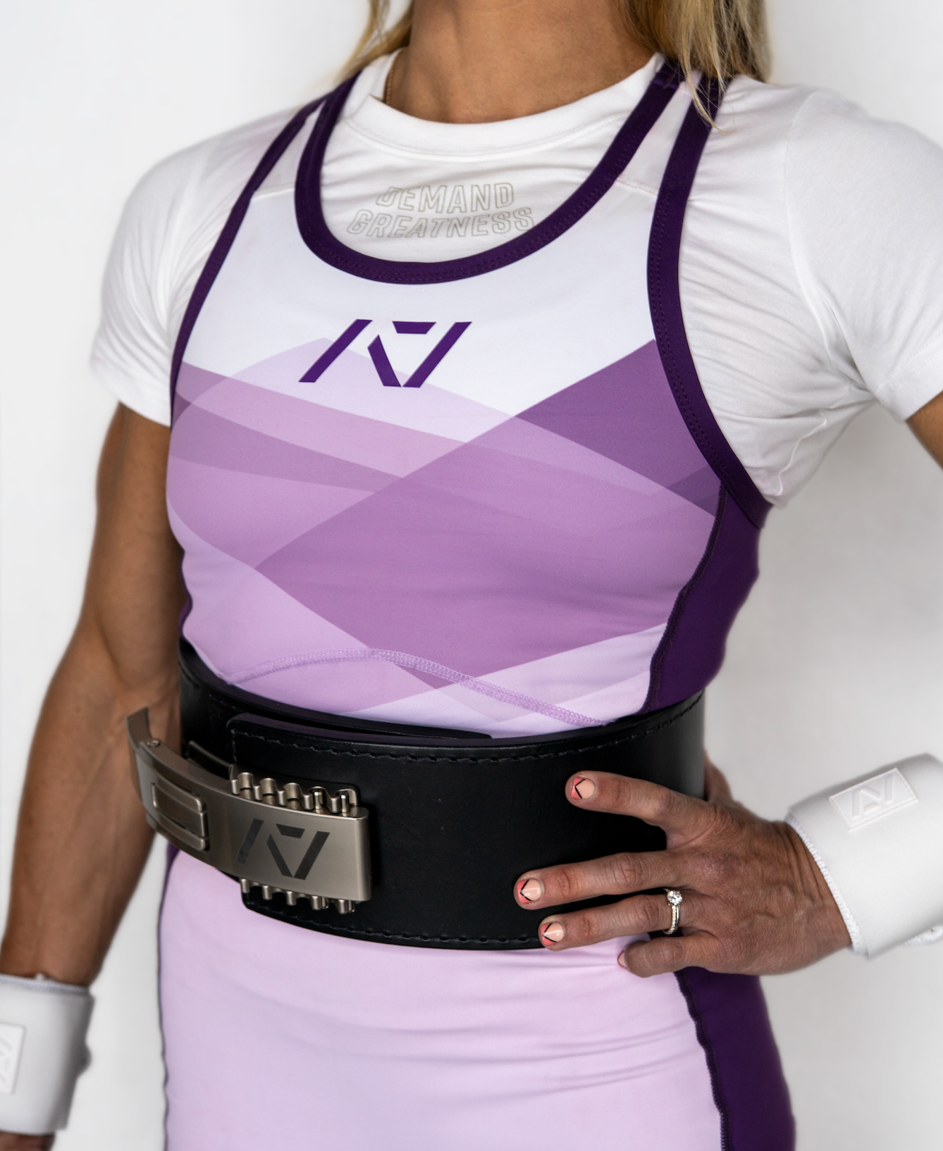 Person wearing a white and purple IPF Approved singlet with a belt on a plain background