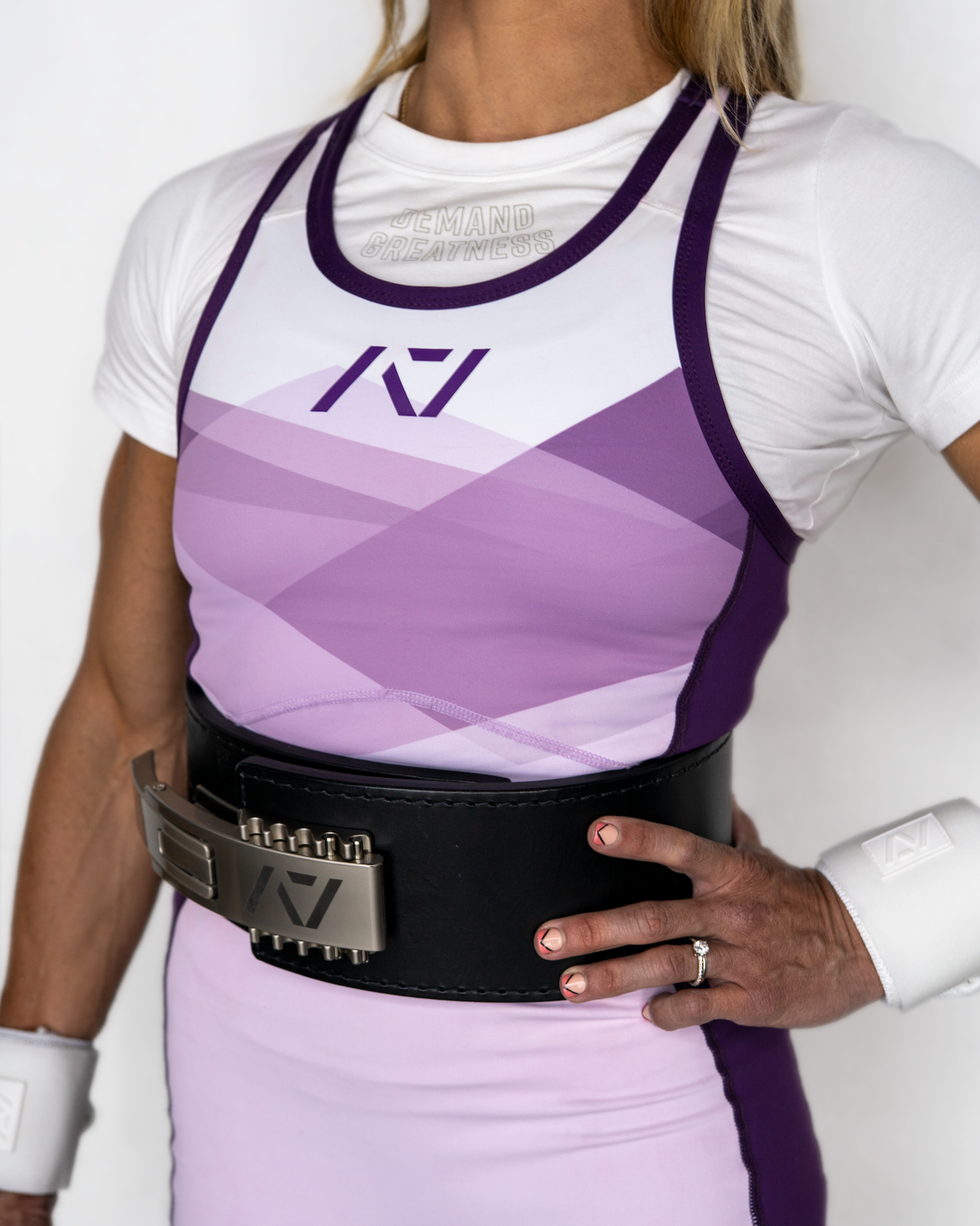 Person wearing a white and purple IPF Approved singlet with a belt on a plain background
