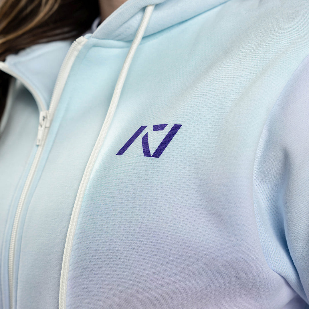 Close-up of the white A7 logo on the Affirmation Zip Hoodie – Pastel, embroidered on soft pink fabric beside a matte zipper for subtle, branded detail.