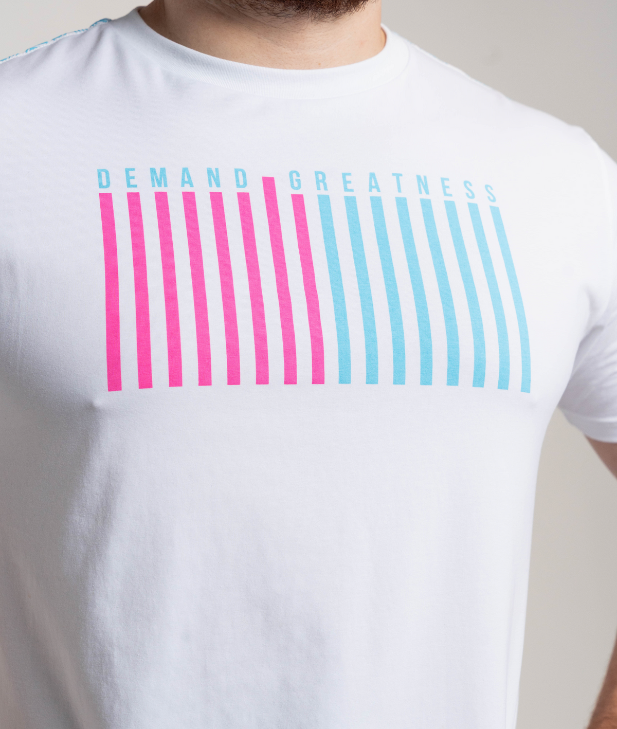 White t-shirt with 'Demand Greatness' text and pink and blue striped design on a plain background