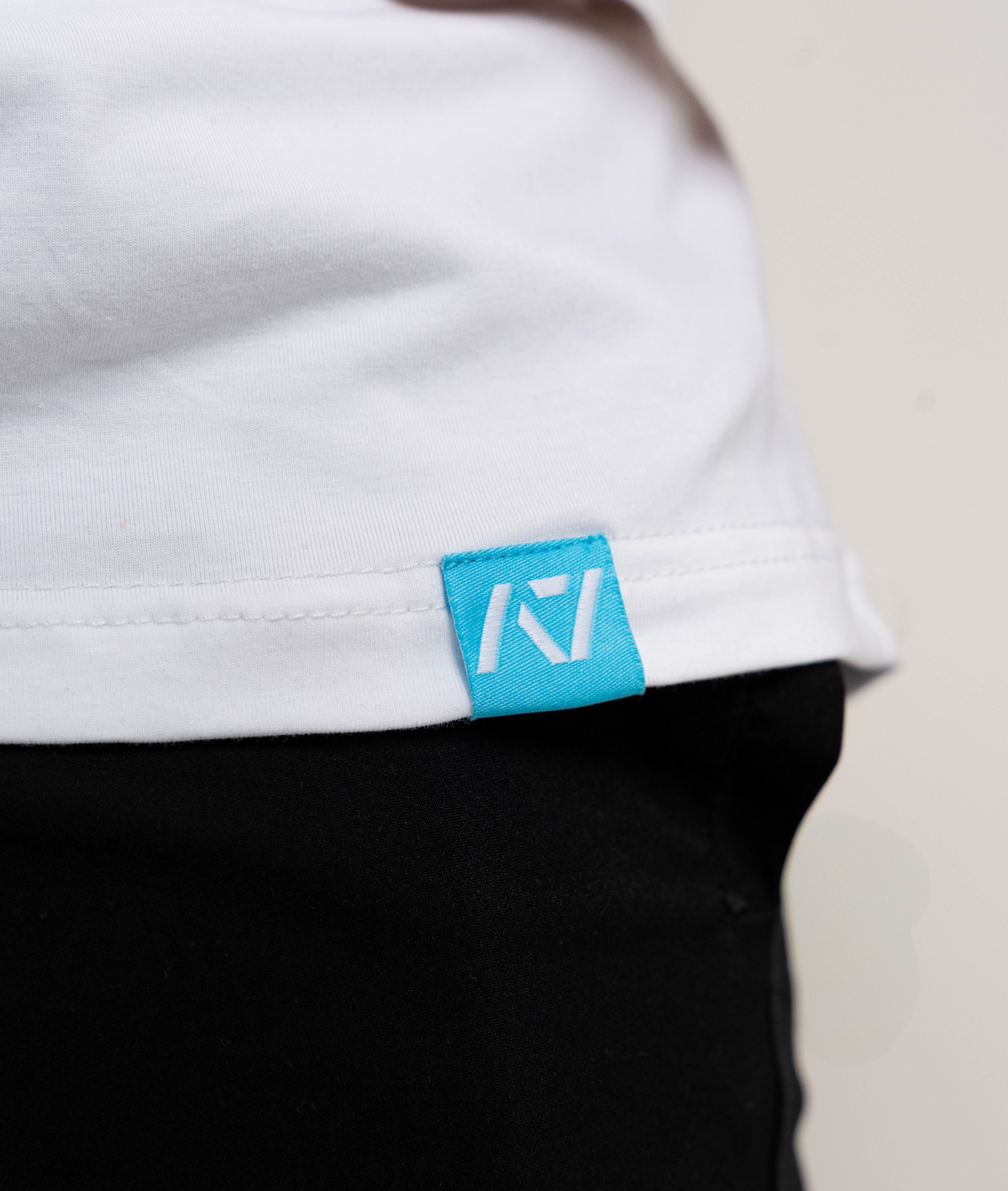 Close-up of a white shirt with a blue logo tag on a neutral background