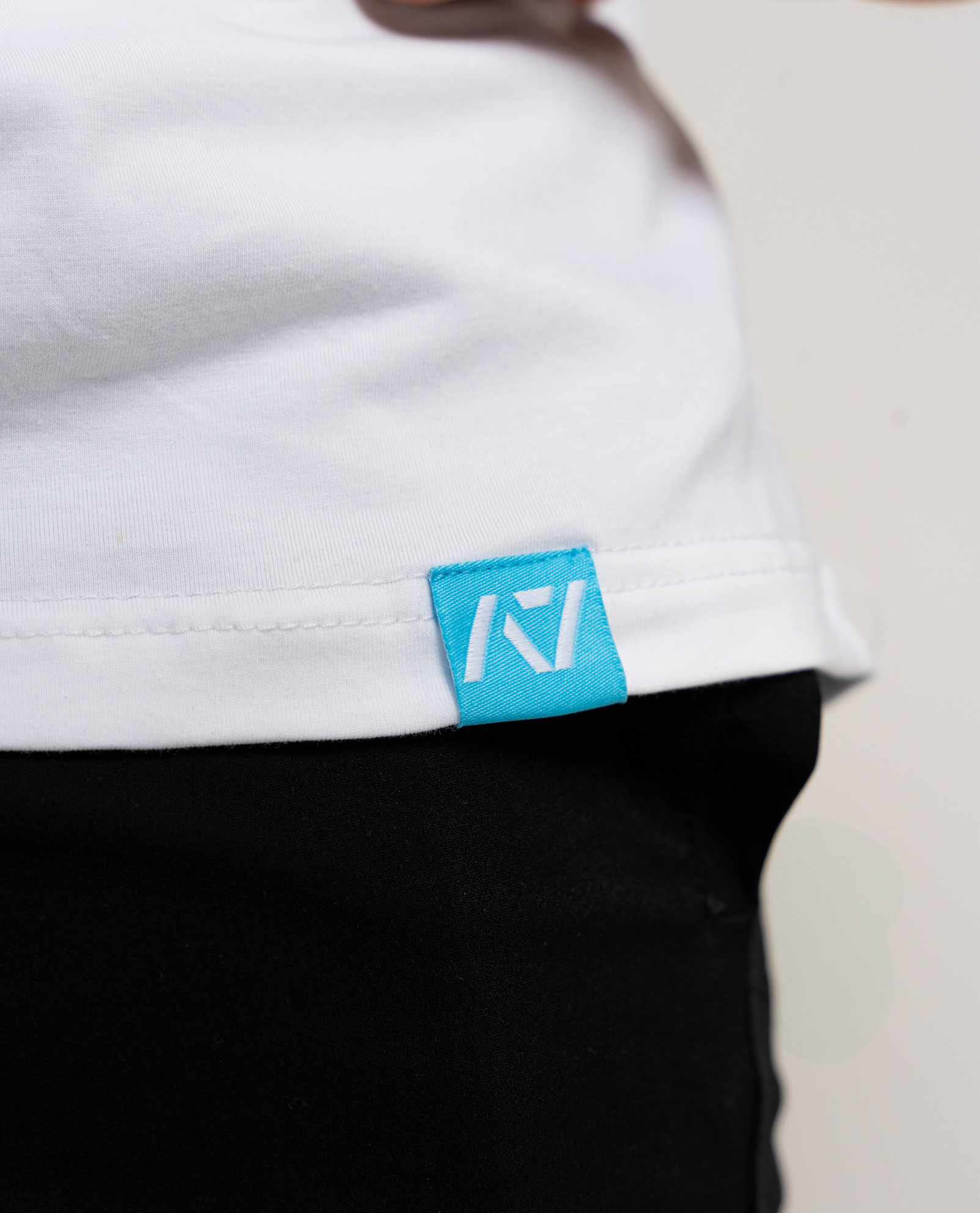 Close-up of a white shirt with a blue logo tag on a neutral background