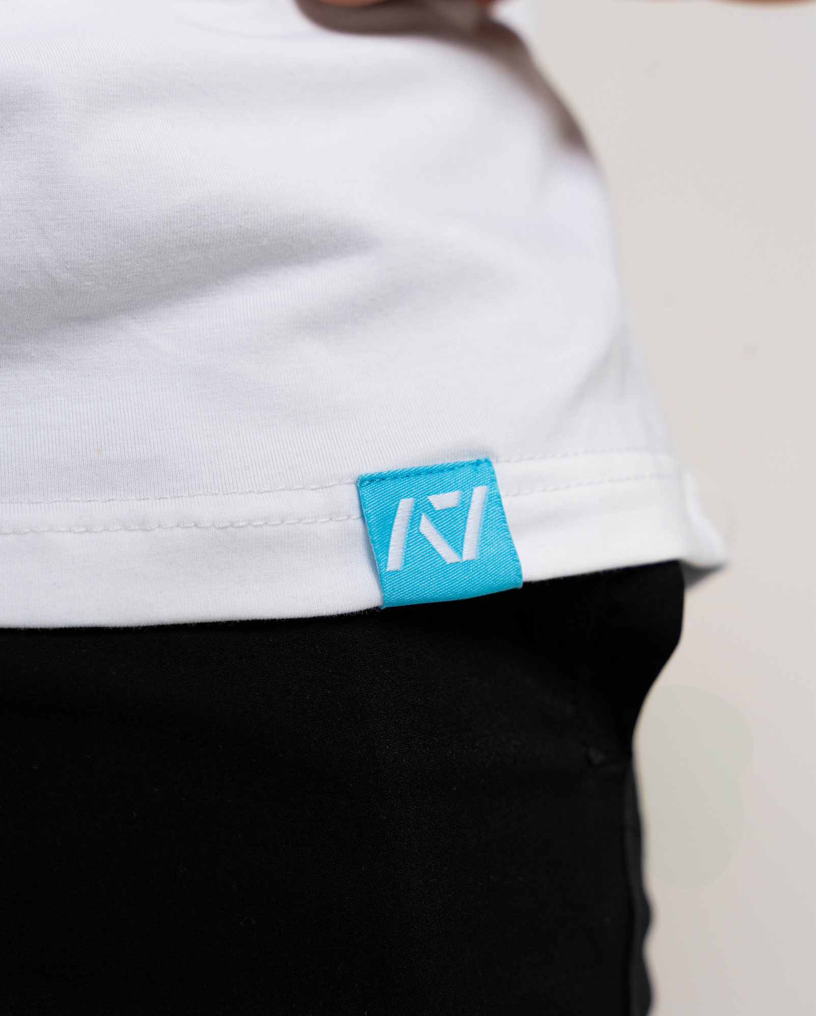 Close-up of a white shirt with a blue logo tag on a neutral background