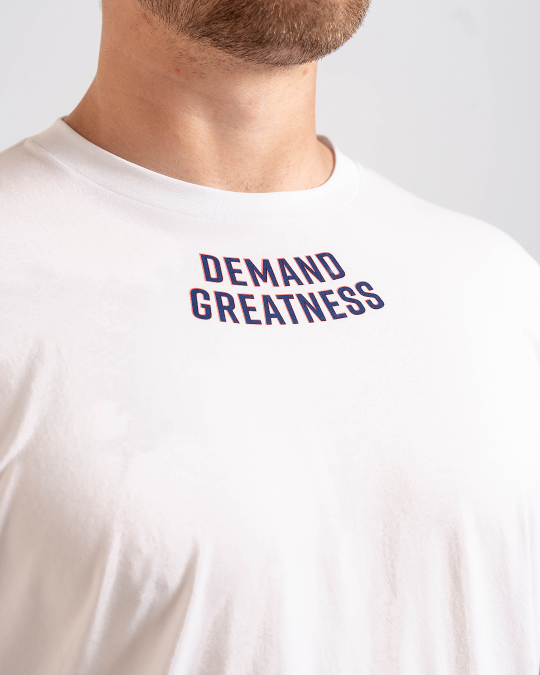 Close-up of the “Demand Greatness” print across the chest of the Americana True-Fit Meet Shirt, featuring bold typography in red, white, and blue.