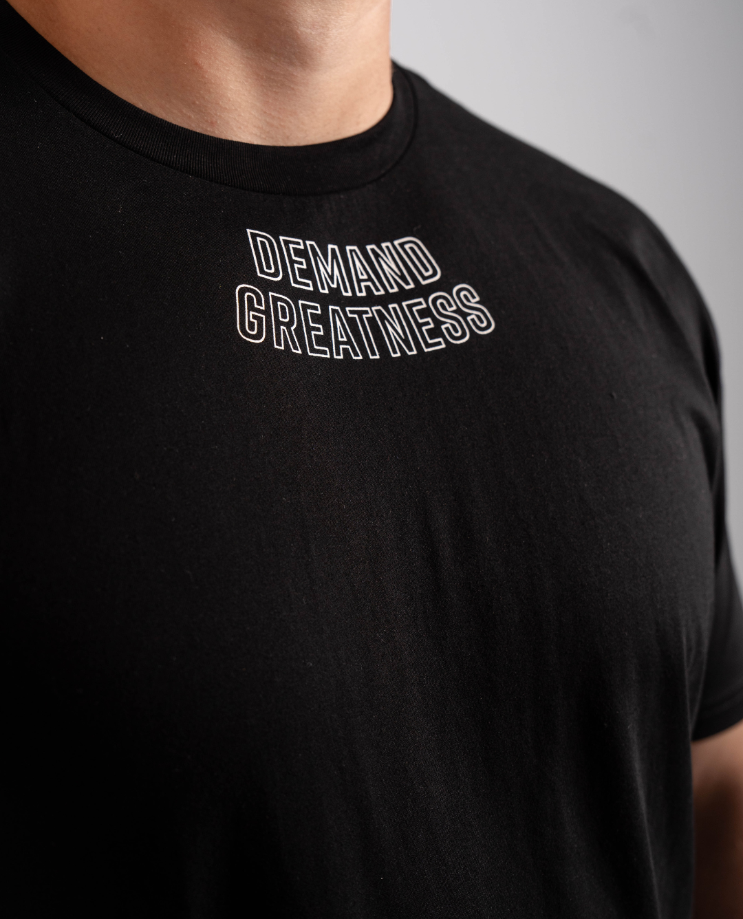 Close-up of “Demand Greatness” print across the chest of the Domino True‑Fit Men’s Meet Shirt, highlighting bold monochrome lettering on soft stretch fabric.