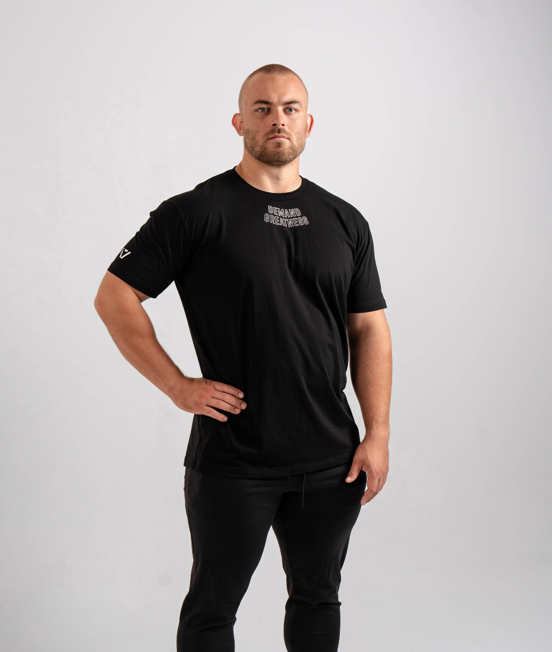 Front view of the Domino True‑Fit Meet Shirt showcasing the “Demand Greatness” print and athletic torso fit.