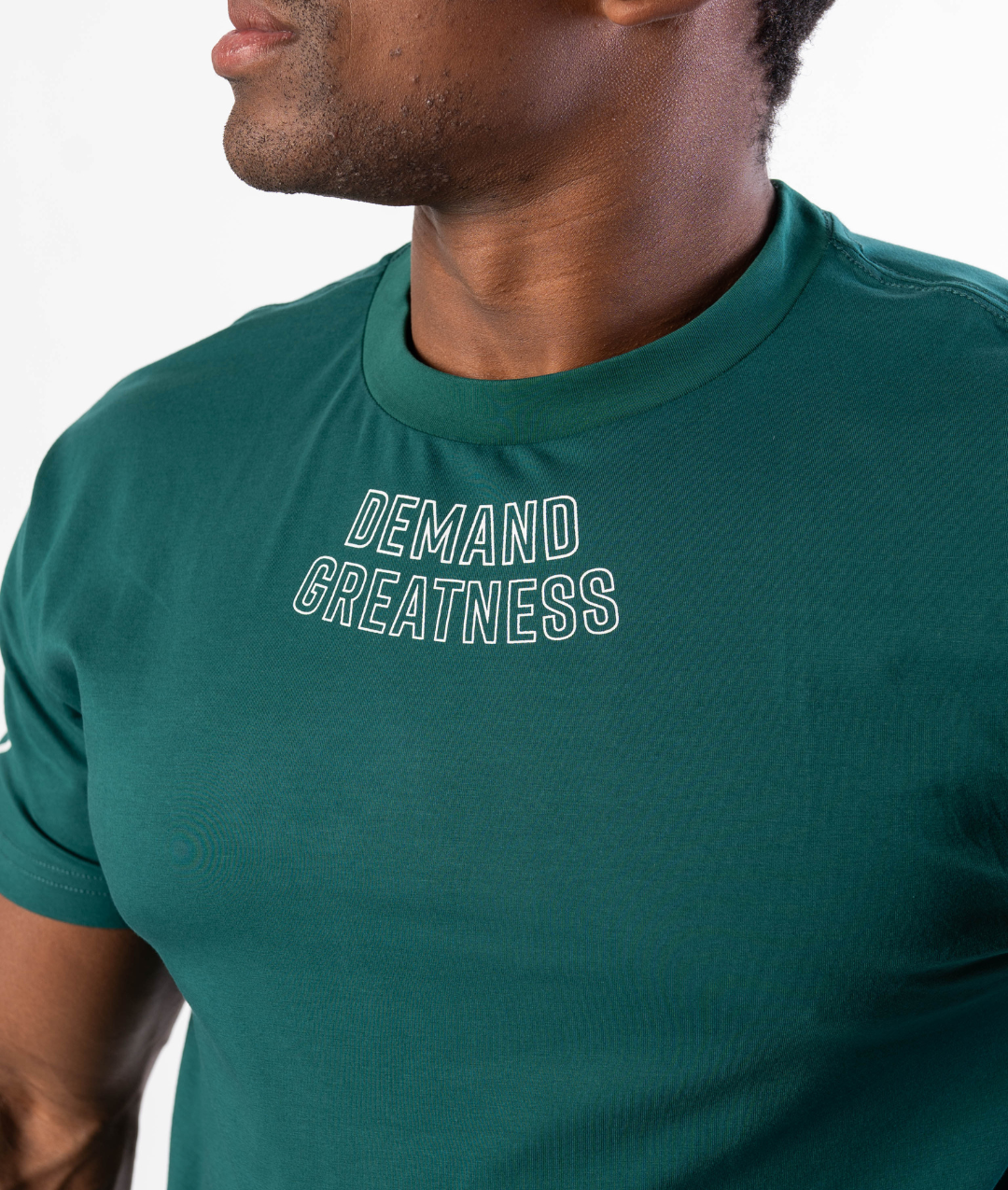 Close-up of “Demand Greatness” chest print on the Emerald Forás True‑Fit Meet Shirt, with bold white typography contrasting against rich green stretch fabric.