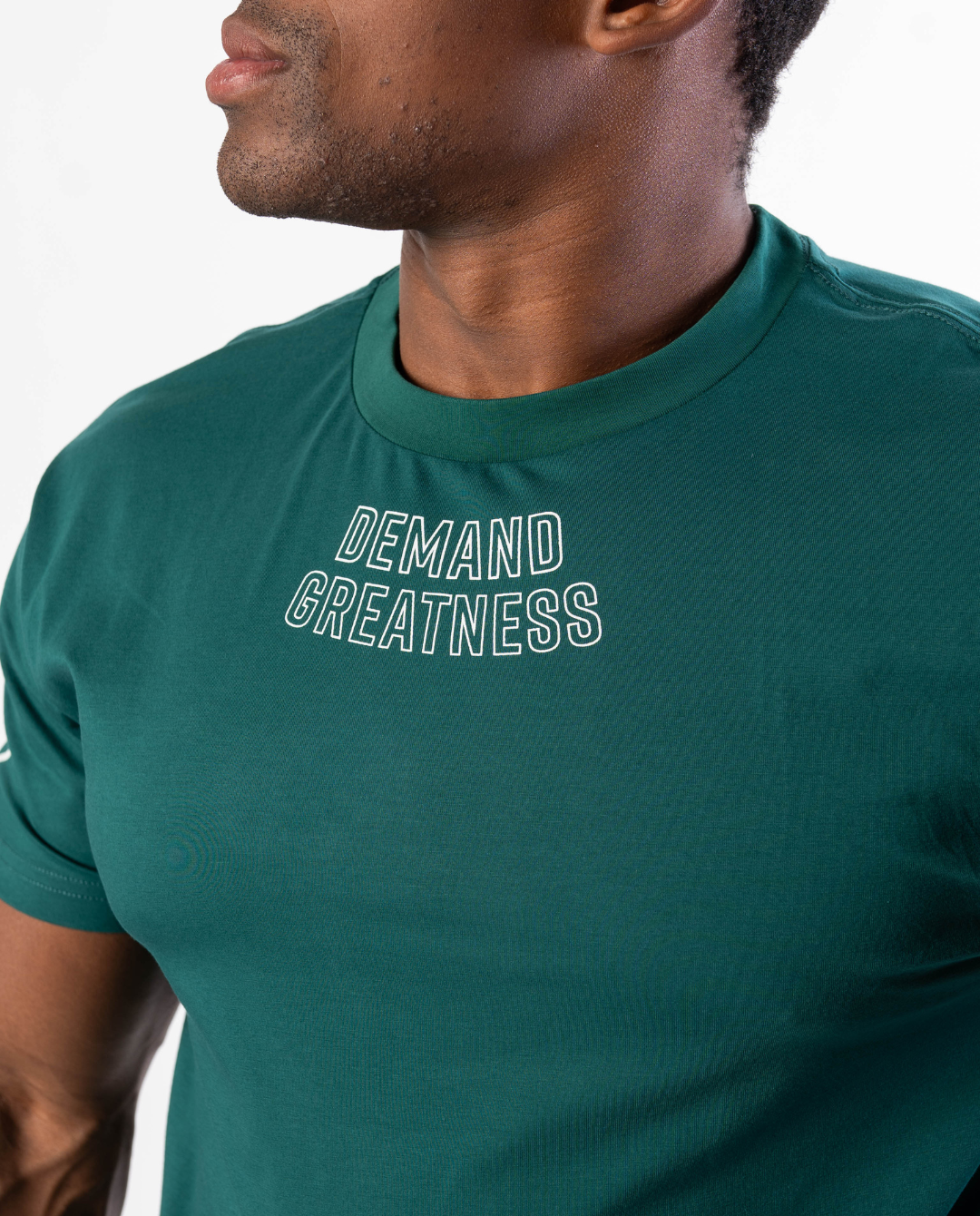 Close-up of “Demand Greatness” chest print on the Emerald Forás True‑Fit Meet Shirt, with bold white typography contrasting against rich green stretch fabric.